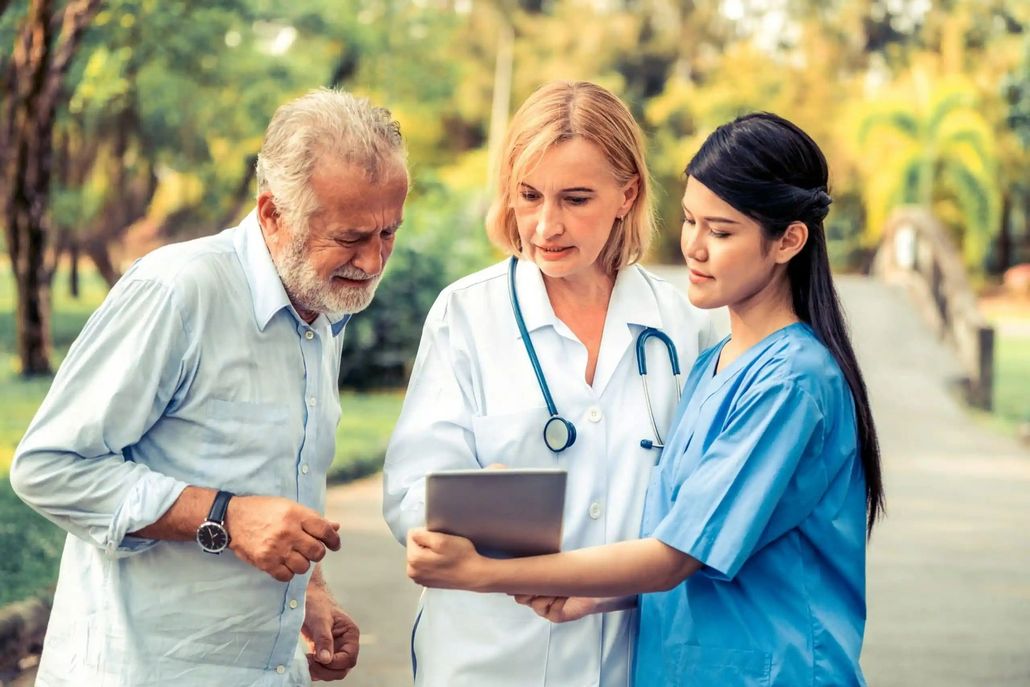 Doctor and nurse showing tablet to older patient outdoors in park setting.