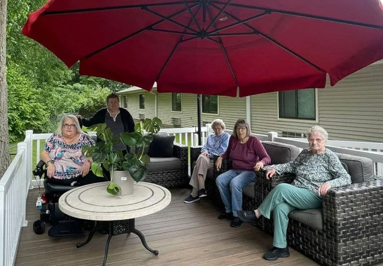 Five people seated on a deck under a red umbrella. One person is in a wheelchair.