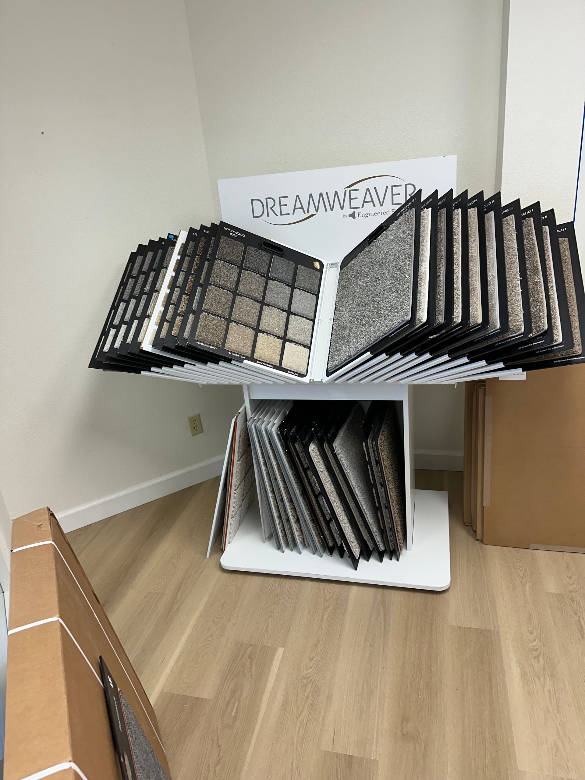 Display of carpet samples on a white rotating stand in a showroom with cardboard boxes.