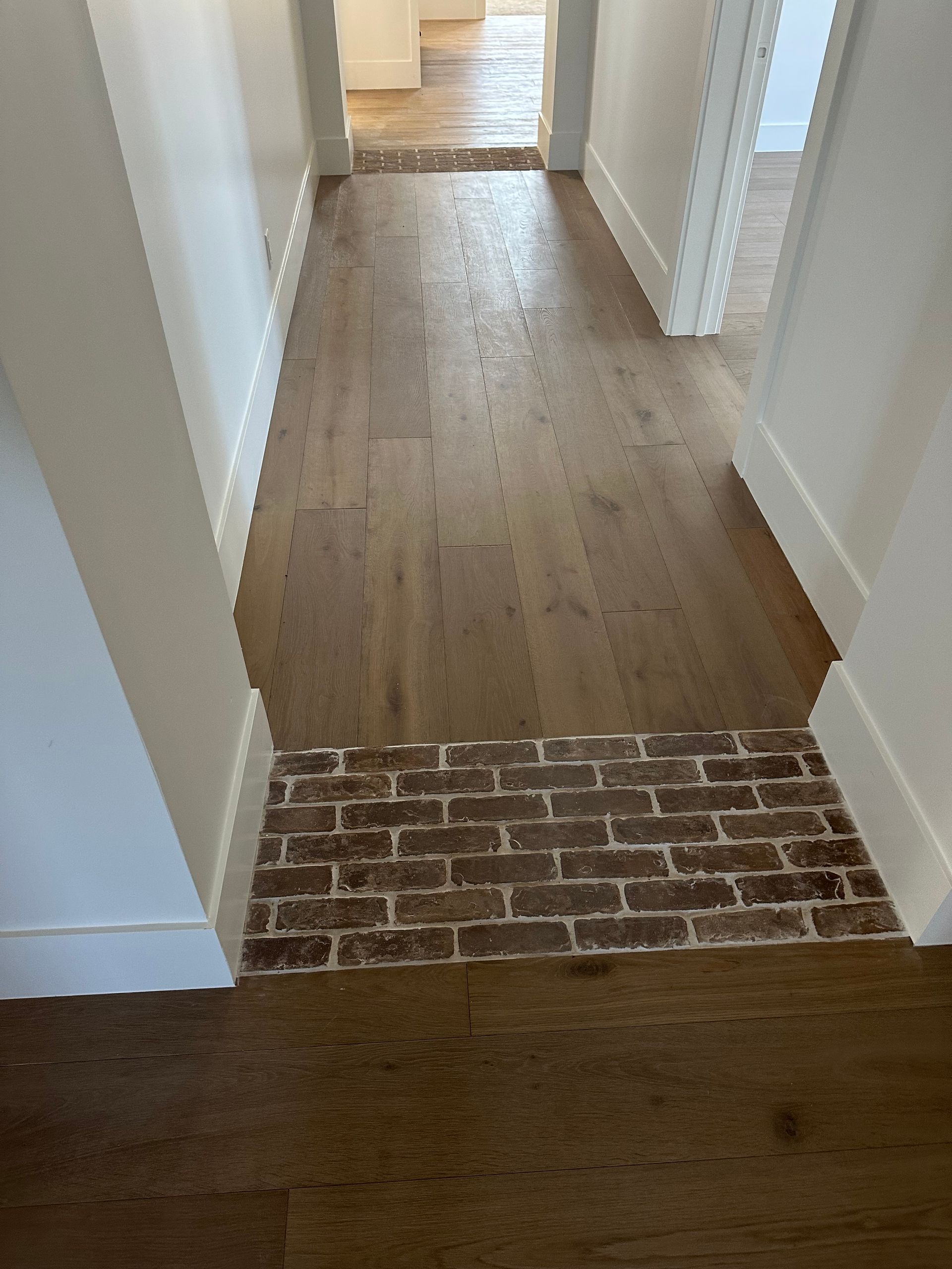 Hallway with hardwood floors, brick section, white walls, and doorways.