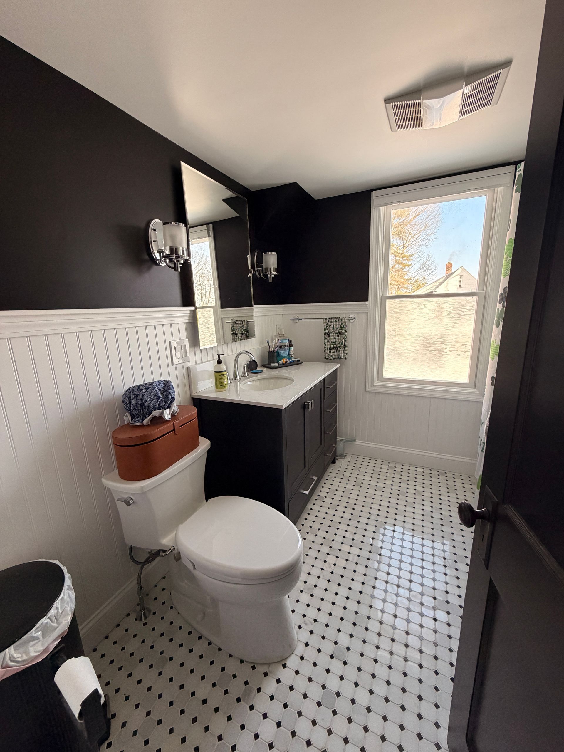 Small black-and-white bathroom with toilet, vanity sink, mirror, and window.