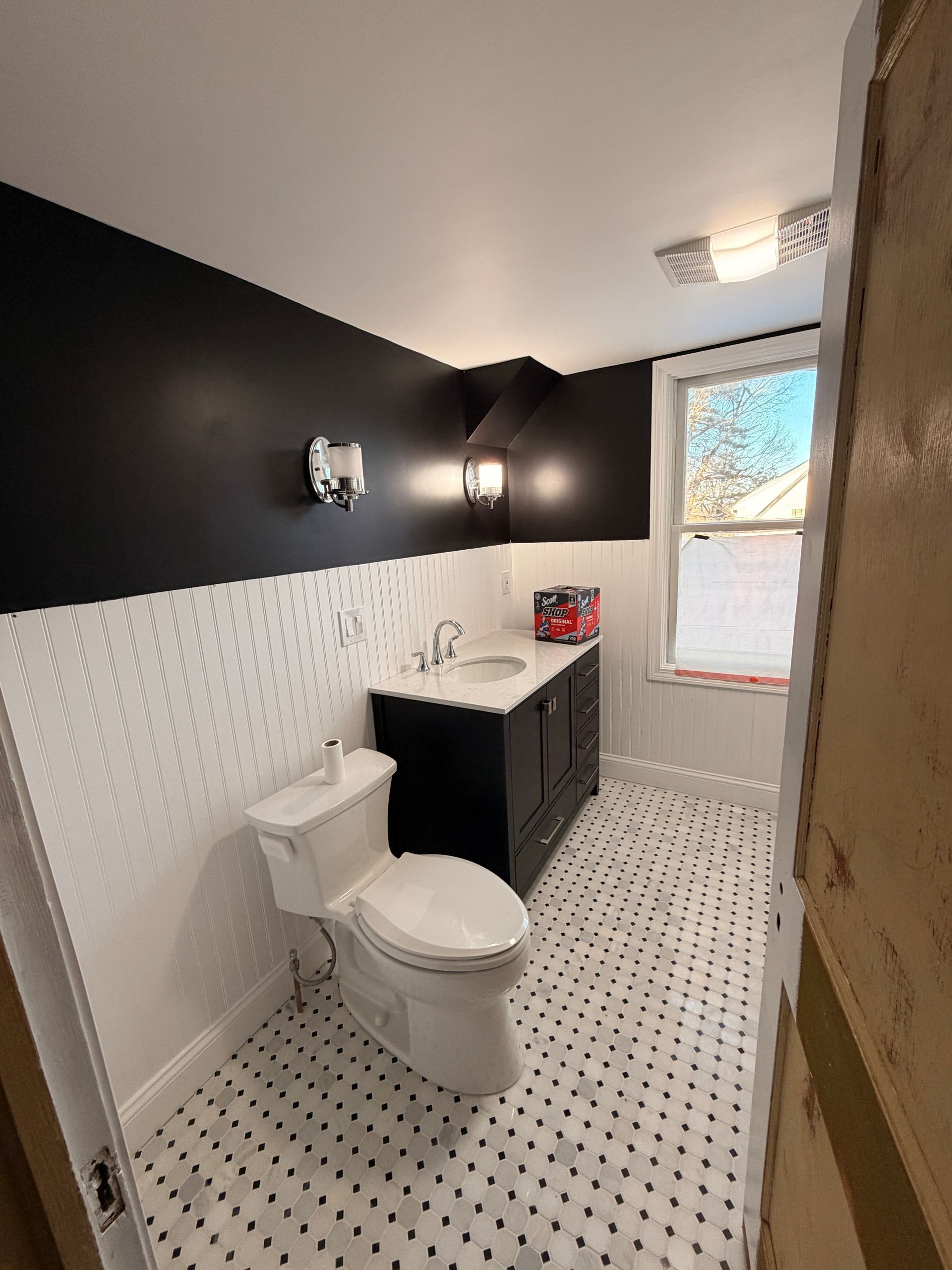 Small bathroom with black-and-white decor, toilet, vanity, and window light