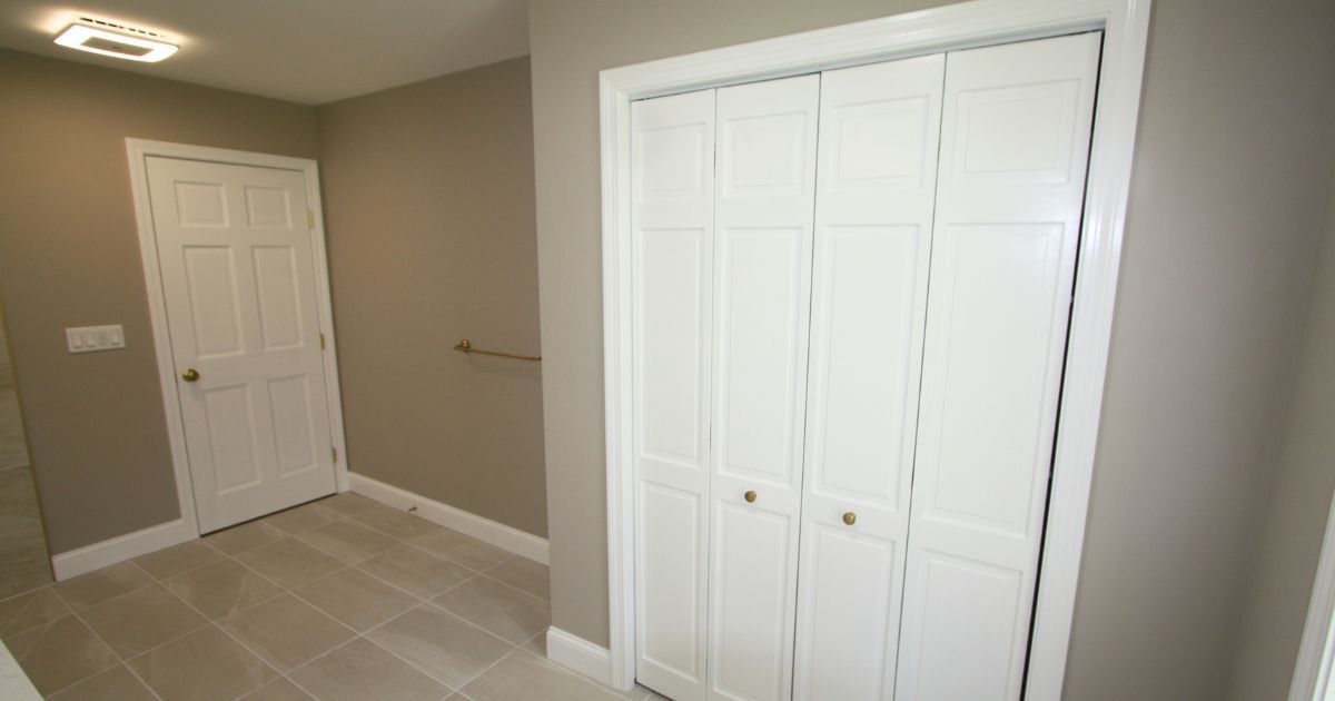 Empty beige bedroom with white closet doors, a white entry door, and tiled floor.