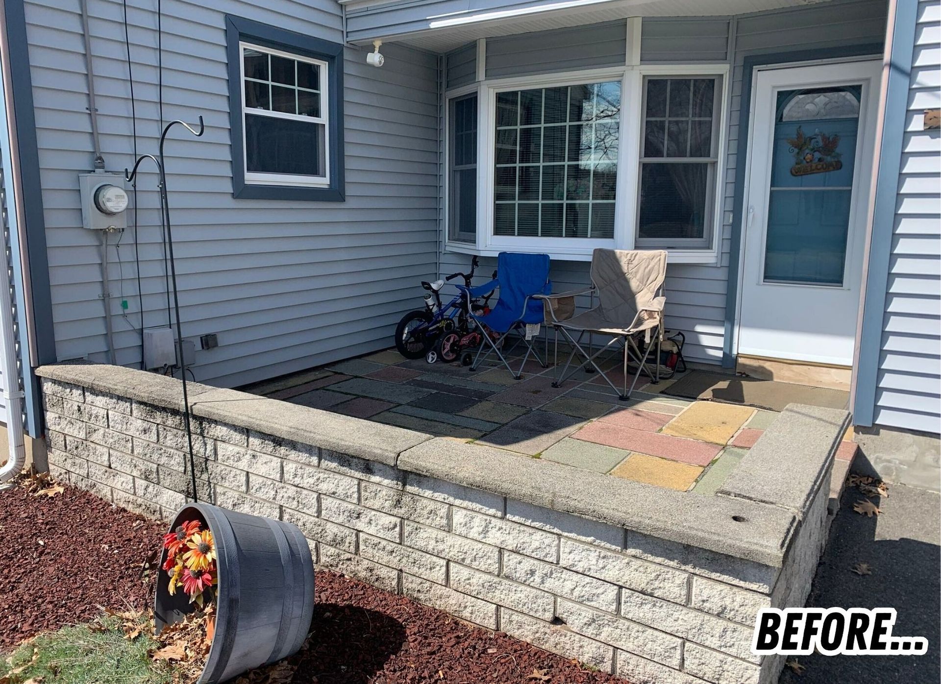 Front porch with gray siding, concrete half-wall, blue door, chairs, and a patio; BEFORE text in corner