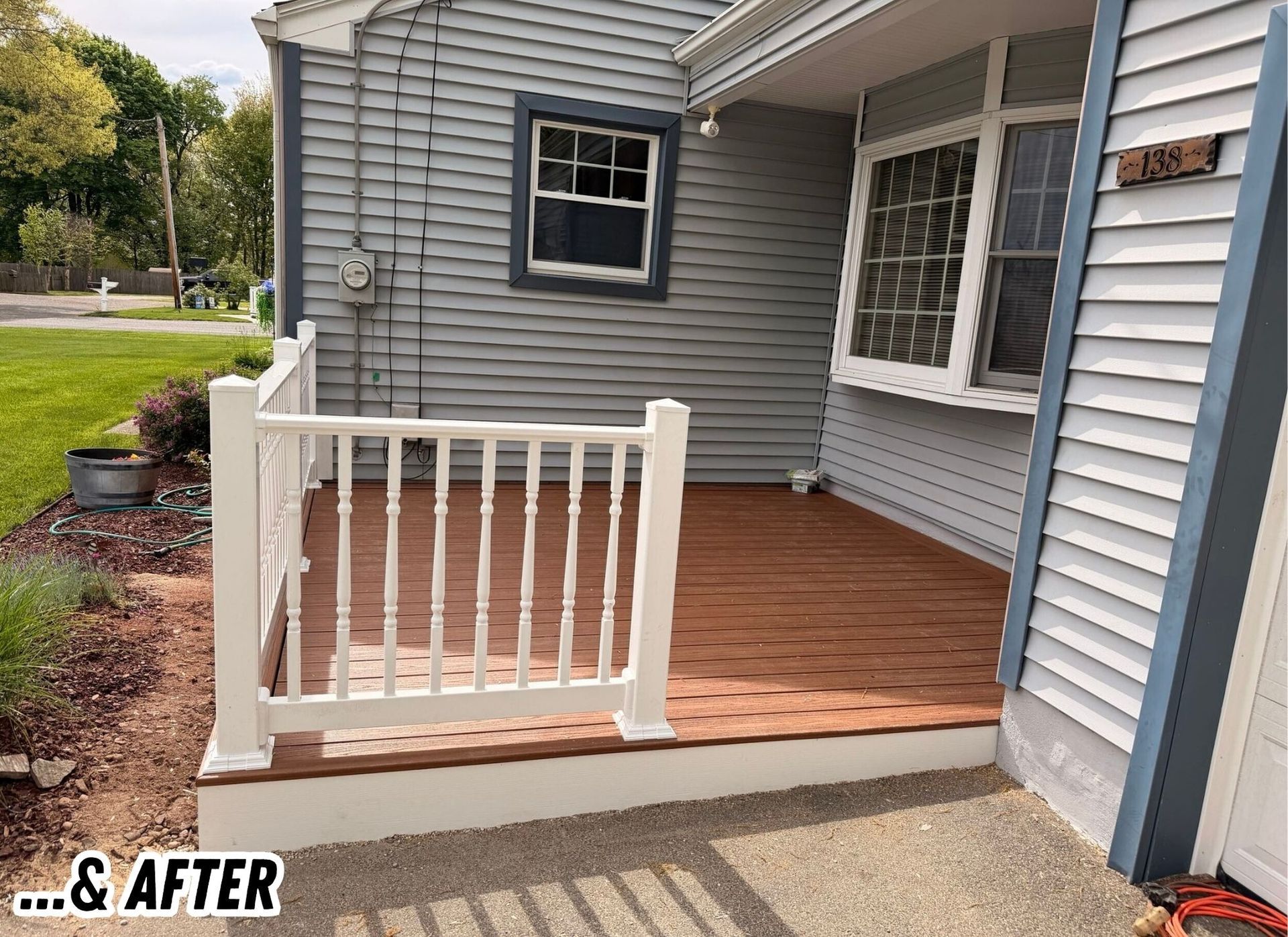 Small front porch with new wood decking, white railing, and gray siding next to a house.