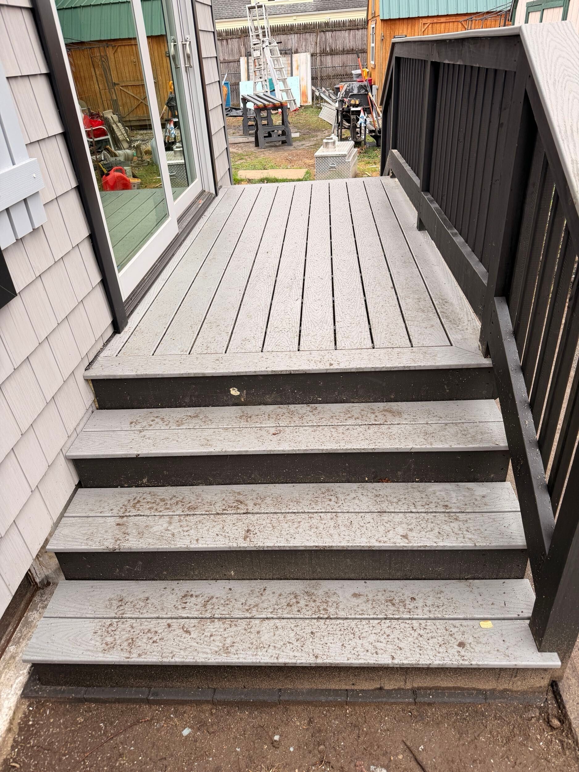 Stairway leading to a wooden deck with black railings and a yard visible beyond.