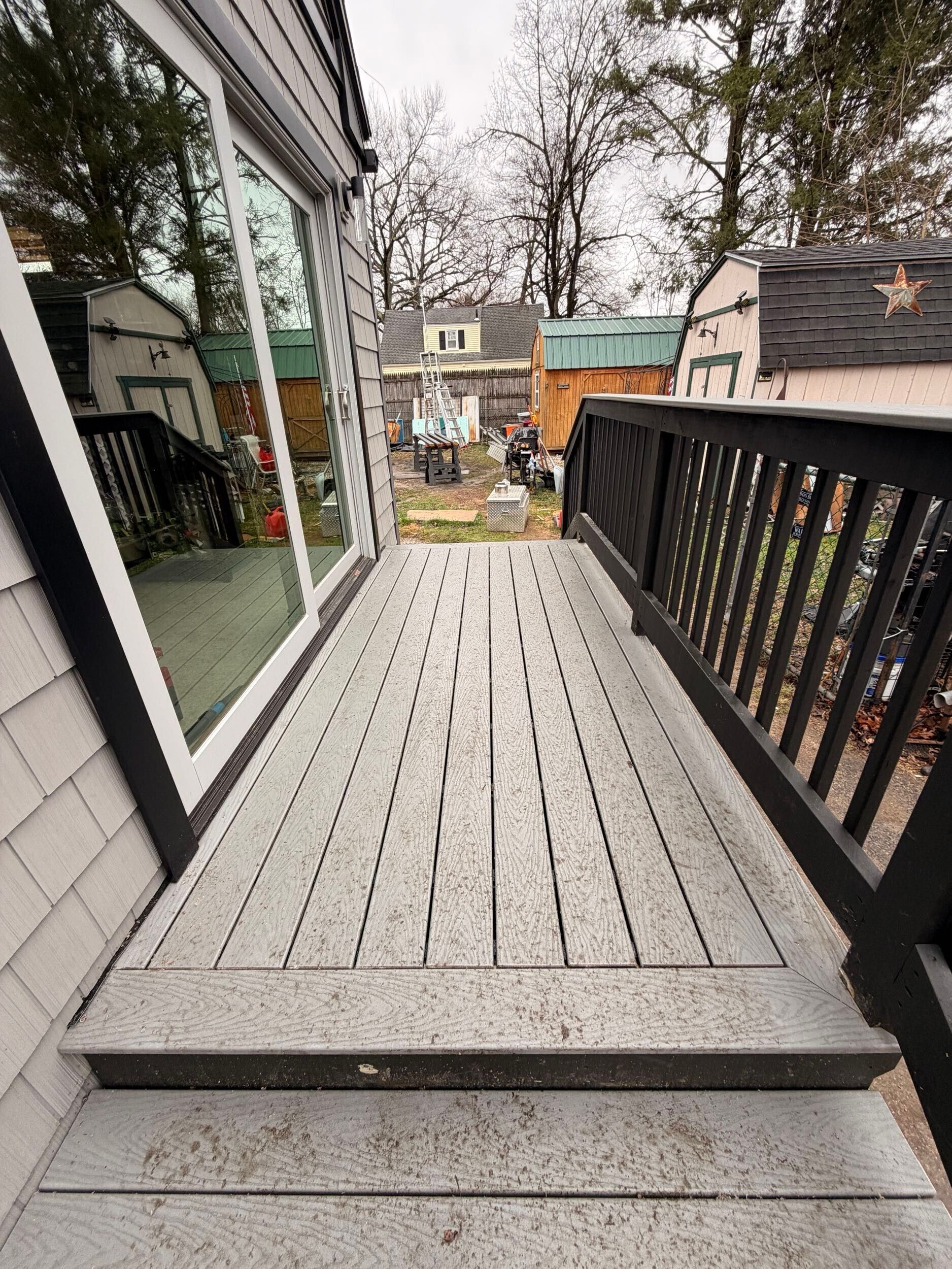 Wooden deck stairs leading to a narrow backyard balcony with black railing and houses beyond.