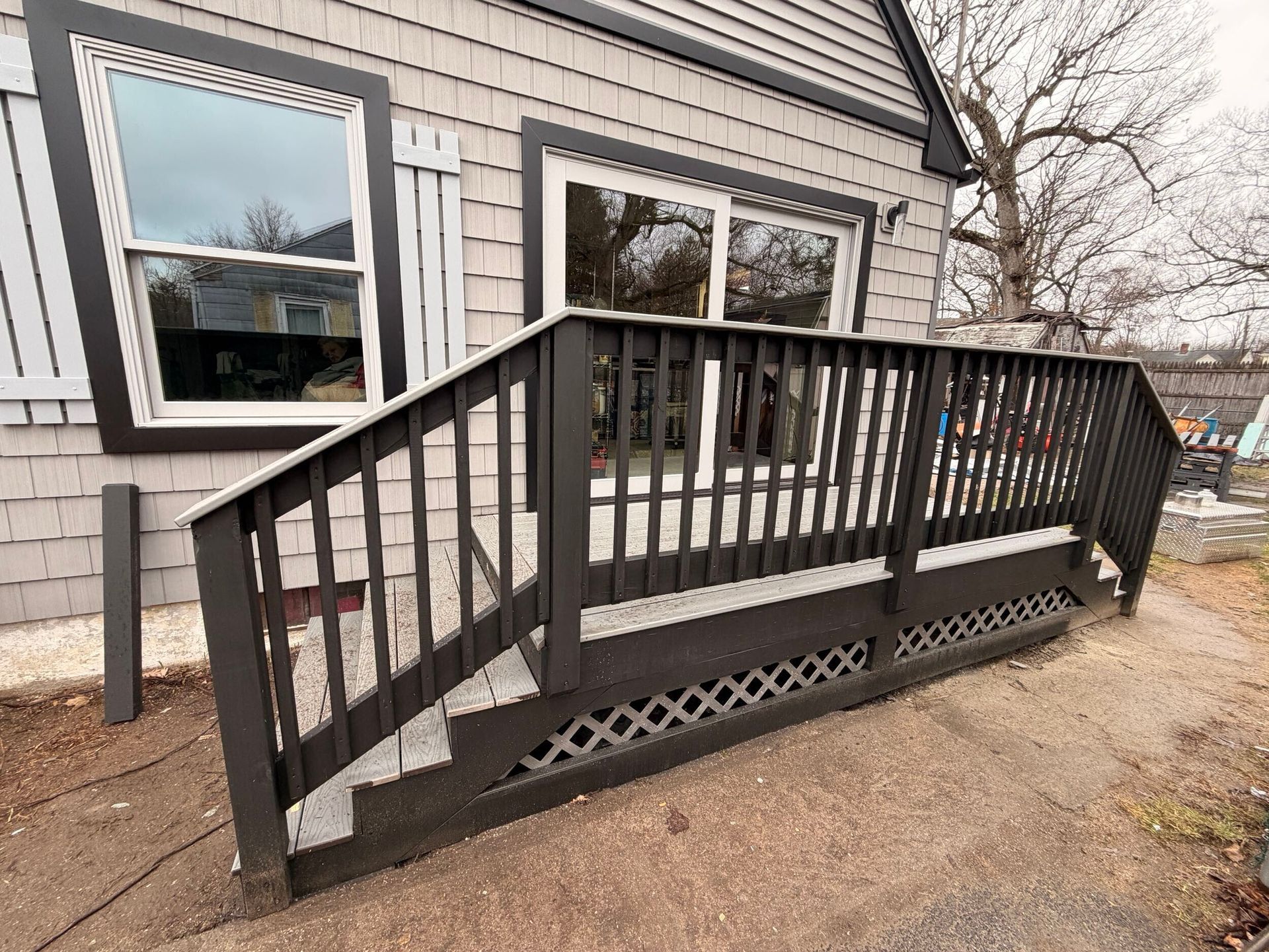Black wooden accessibility ramp with railings beside a house exterior