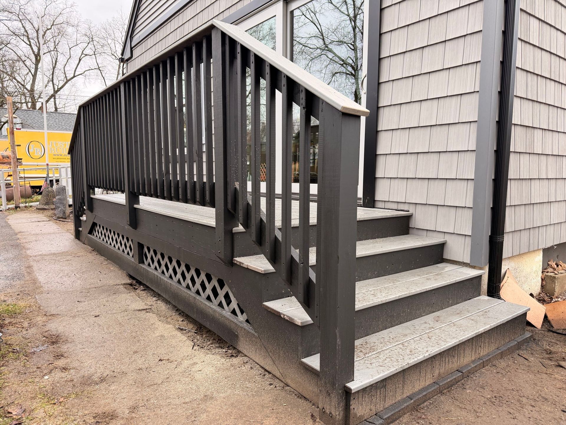 Exterior wooden stairs with black railing and lattice skirting beside a gray house