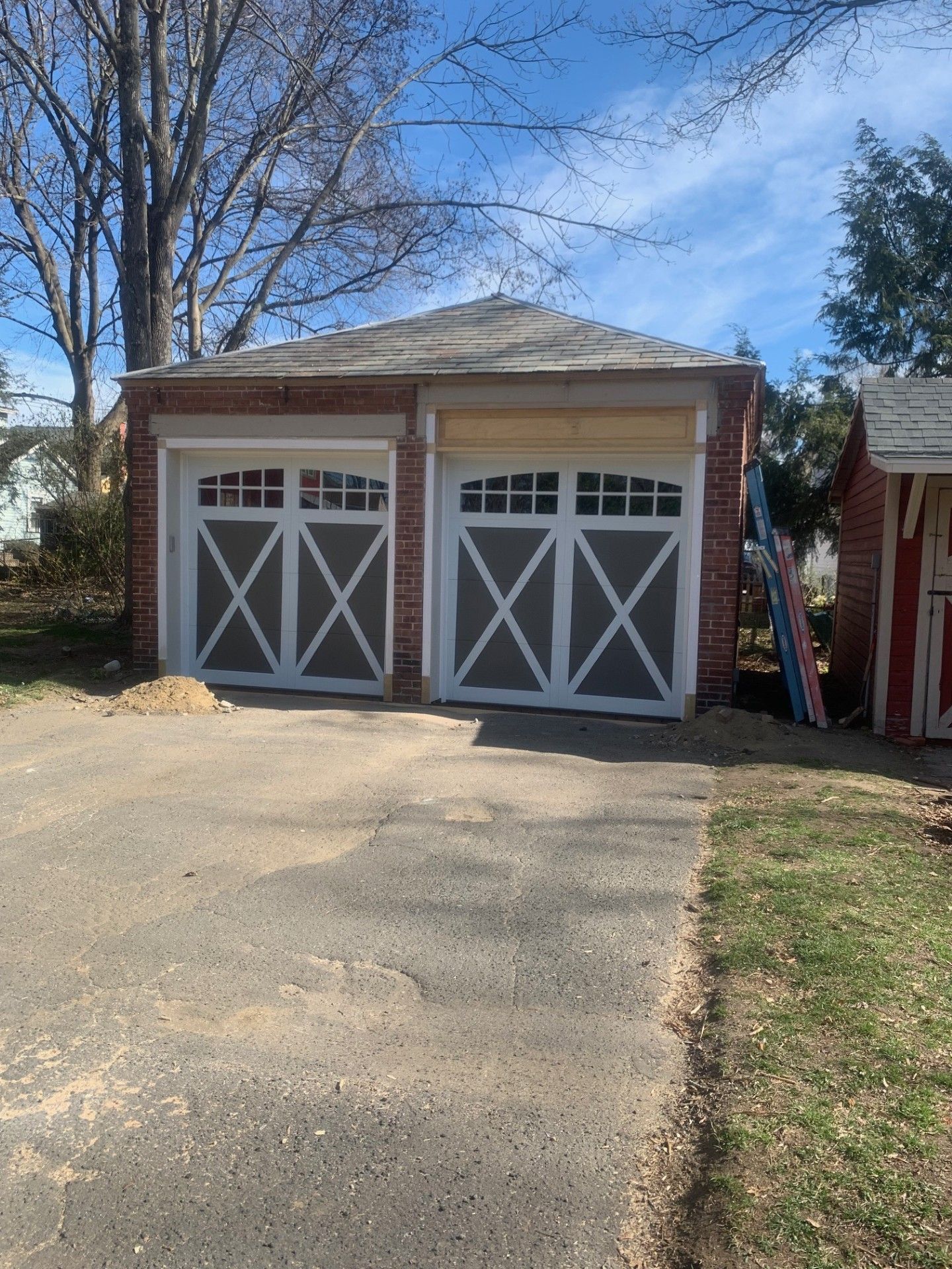 Two-car garage with white doors, gray panels, and red brick facade on a sunny day.