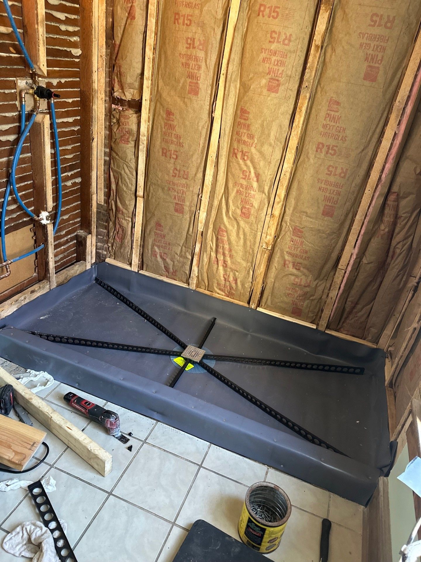 Shower installation with a gray pan, black drainage, and exposed wood framing.