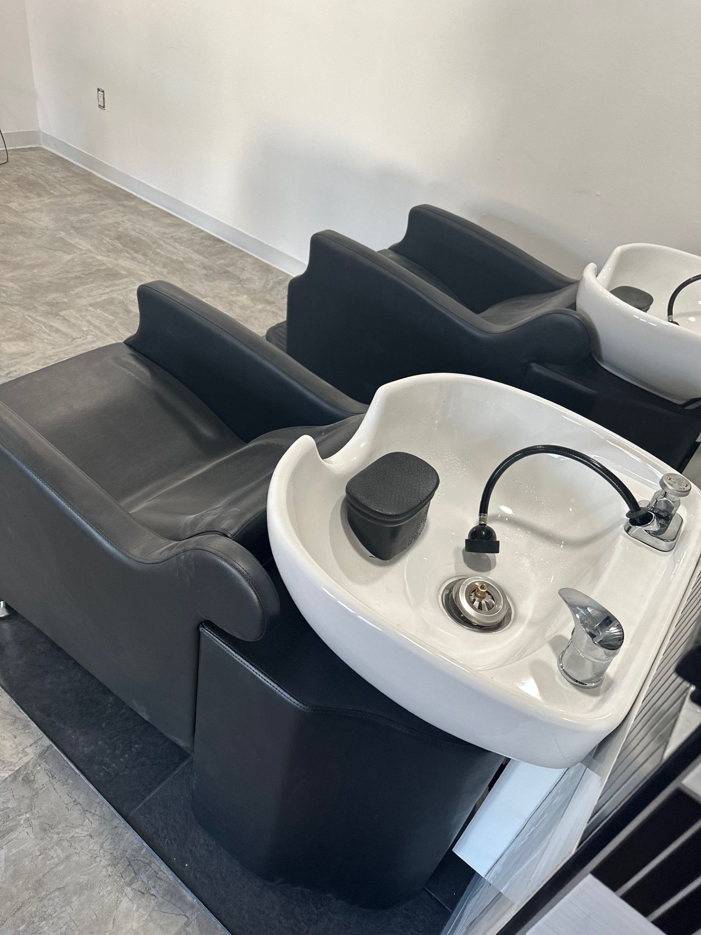 Salon shampoo stations with black chairs, white sinks, and fixtures.