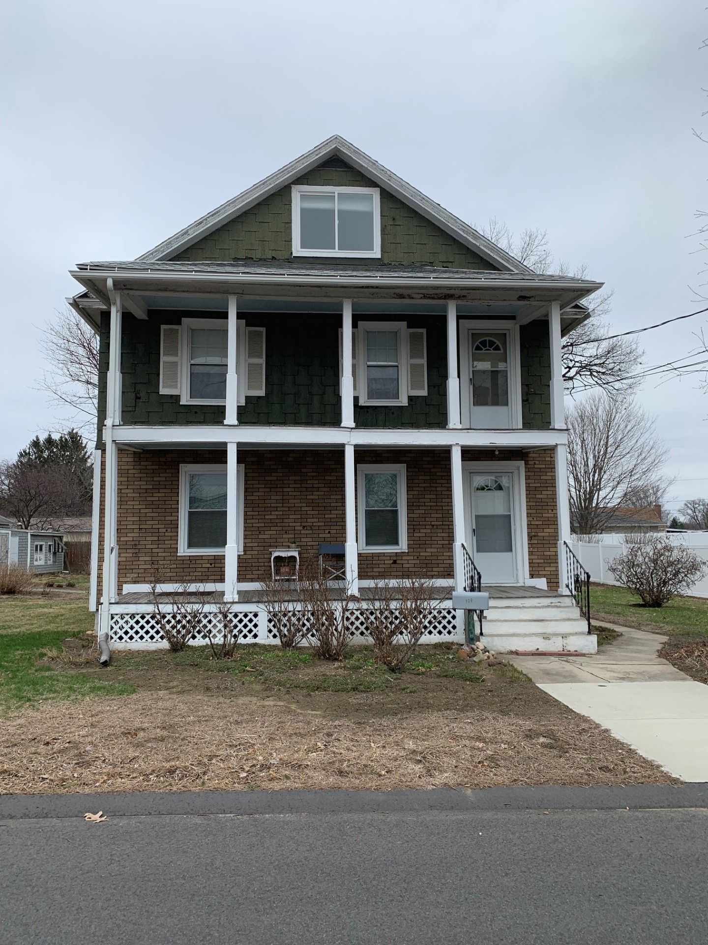 Two-story house with green siding, brick facade, white trim, and a porch. Overcast sky.