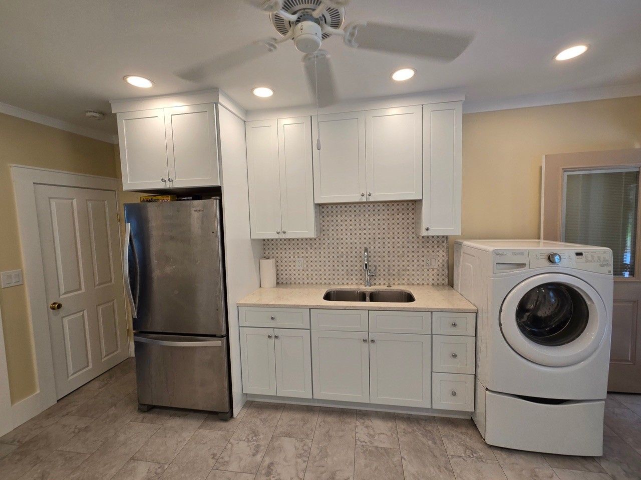 Kitchen with white cabinets, stainless steel refrigerator, sink, washer, and a door.