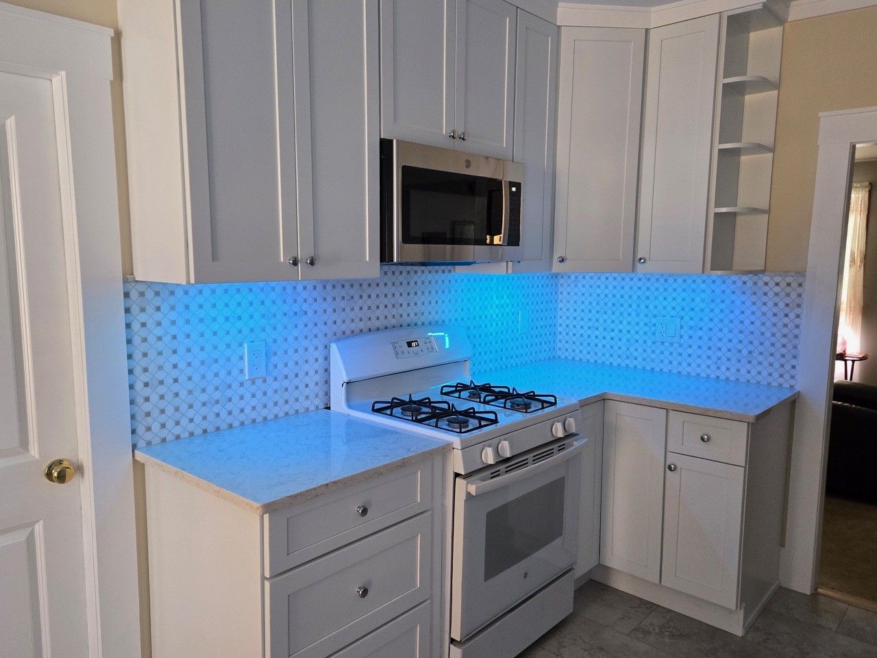 White kitchen with blue LED backsplash lighting; microwave, stove, cabinets, and a door are visible.