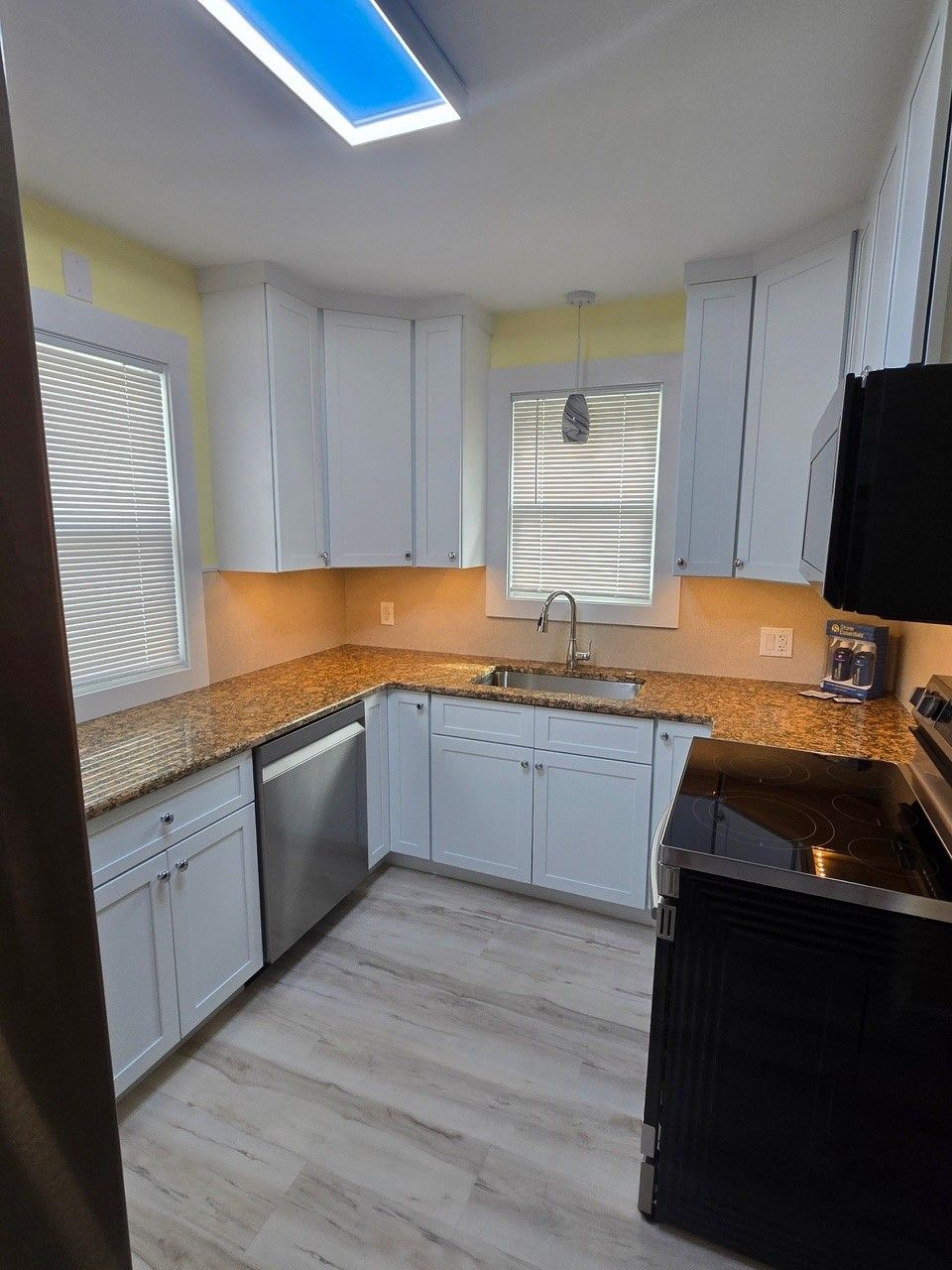 White kitchen with granite countertops, stainless steel appliances, and wood-look flooring.