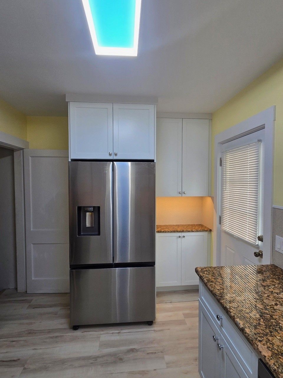 Kitchen with stainless steel refrigerator, white cabinets, and granite countertop. Yellow walls and wood-look flooring.