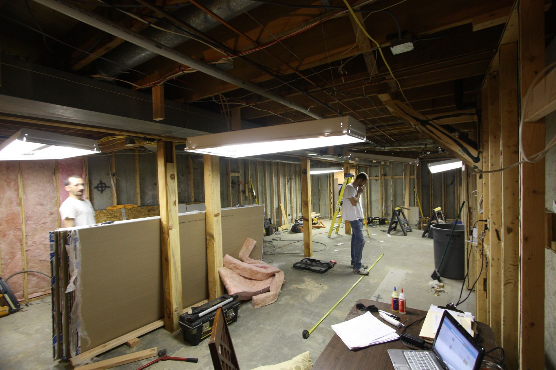 A man is measuring a wall in a basement under construction.
