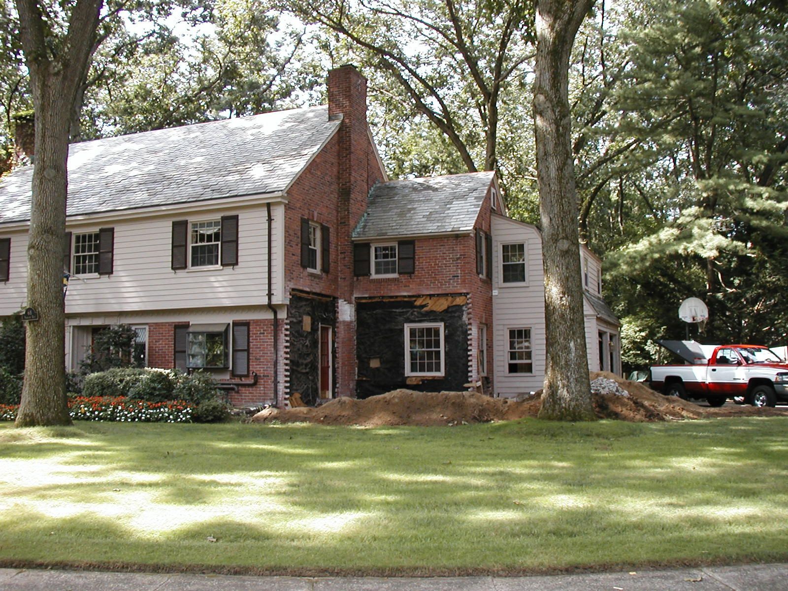 Two-story house undergoing renovation; red brick chimney; pink siding; brown shutters; truck parked in front.