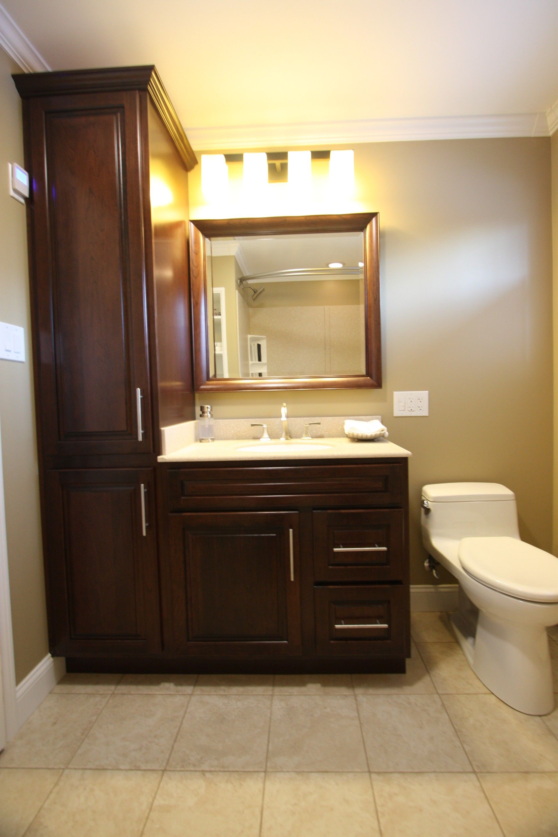 Dark wood bathroom with cabinet, vanity, and toilet on tile floor.