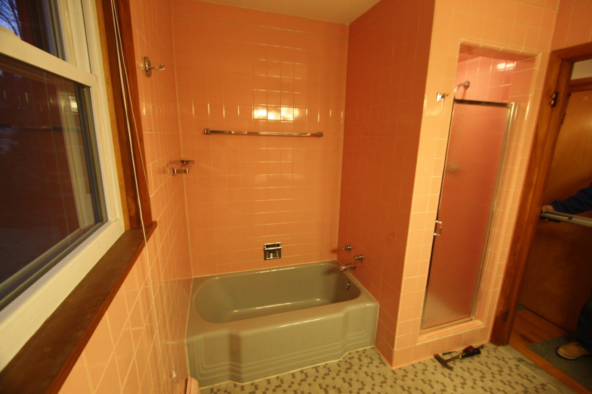 Pink-tiled bathroom with a bathtub, shower, and window. Silver fixtures.