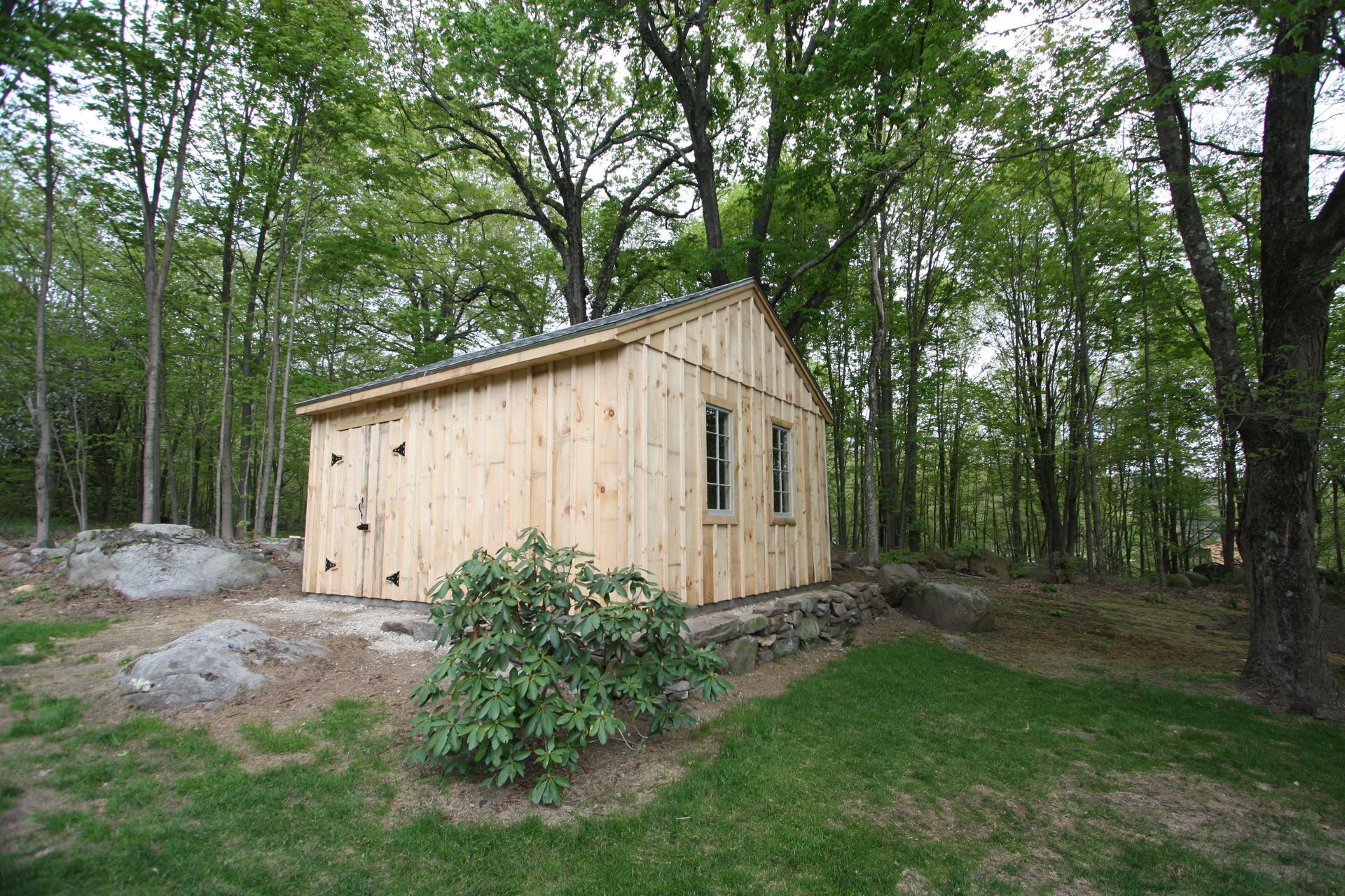 A wooden shed is sitting in the middle of a lush green forest.