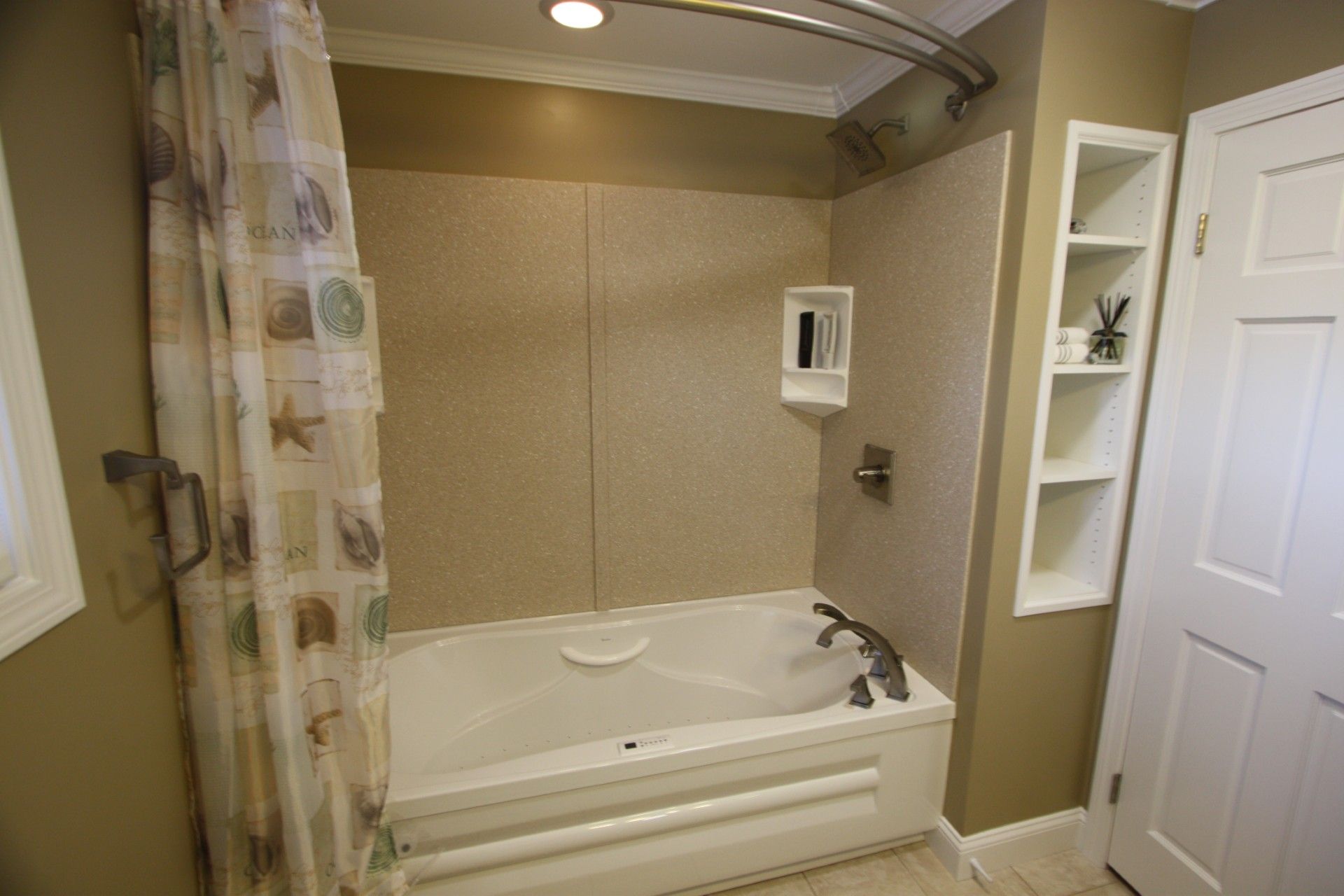 Bathroom with a white bathtub, beige walls, and a built-in shelf. A seashell shower curtain hangs to the left.