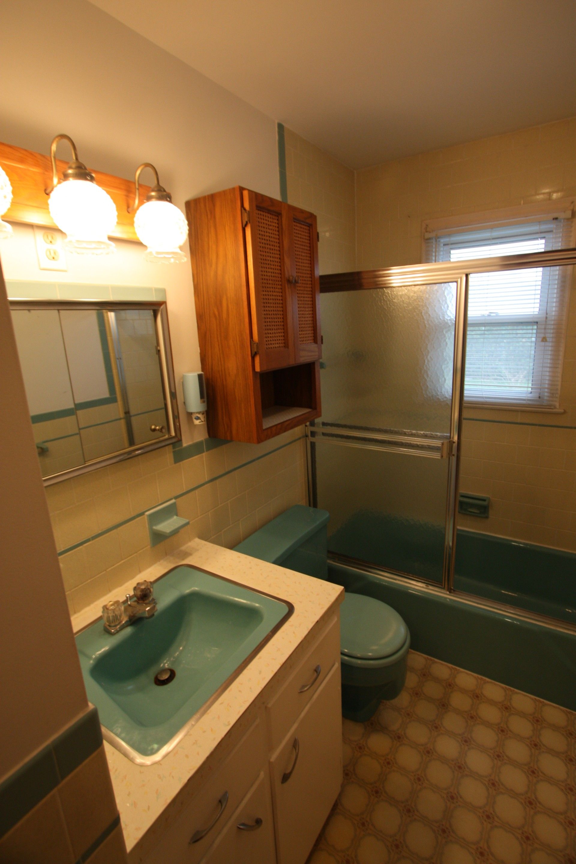 Bathroom with teal fixtures and a wooden medicine cabinet.