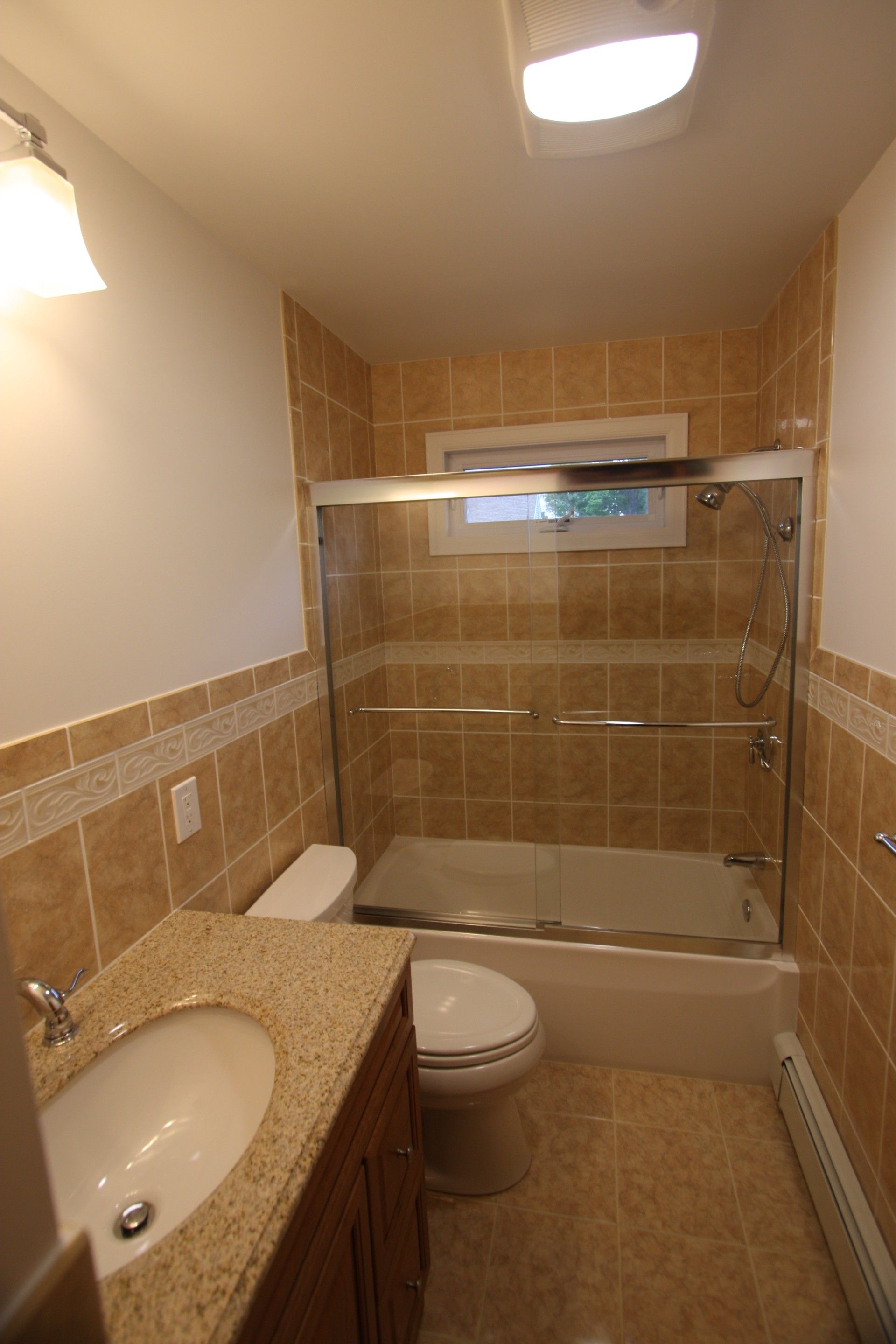 Bathroom with tan tiles, glass shower doors, granite countertop, and a white toilet.