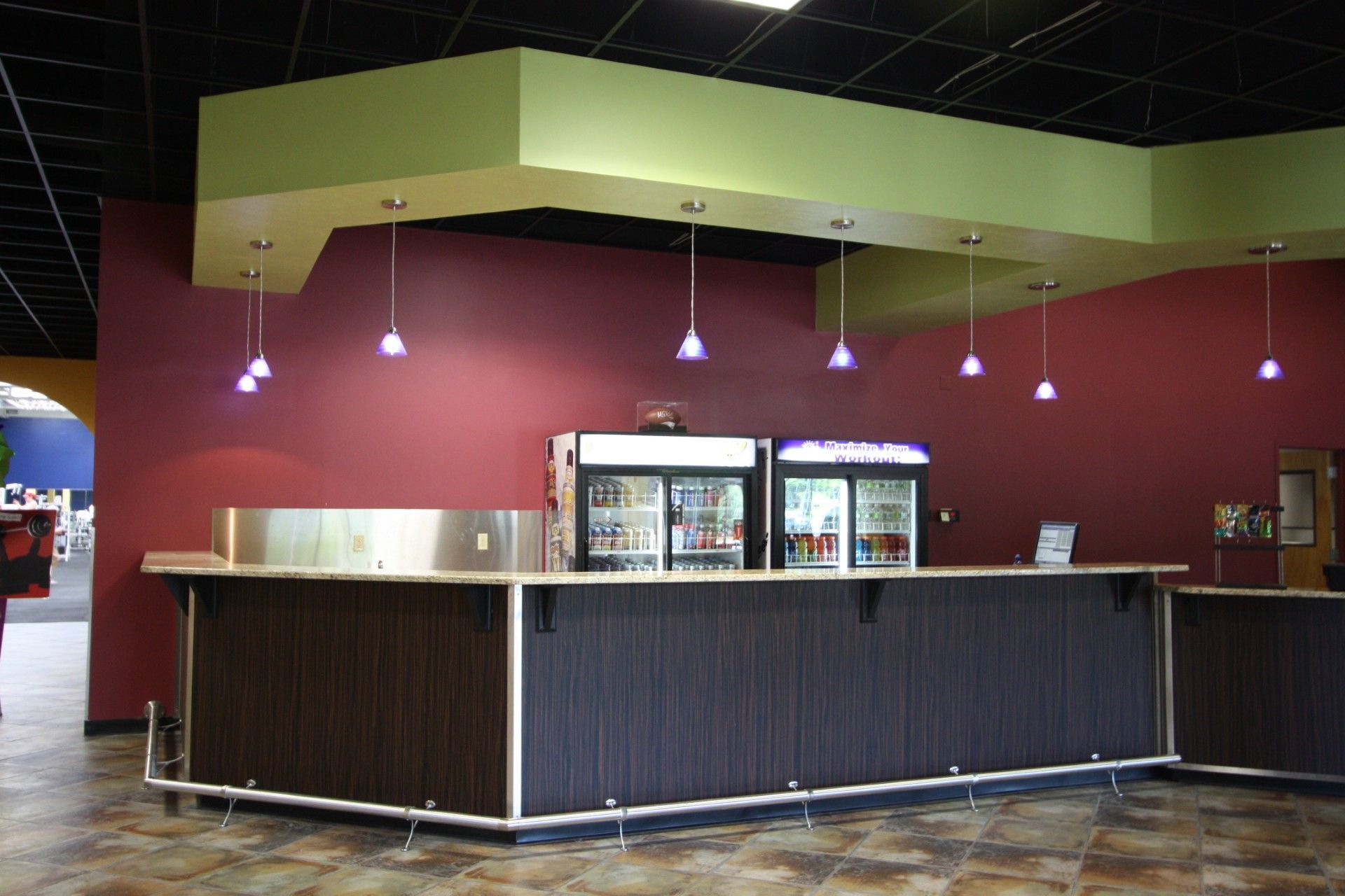 Bar area with a maroon wall and dark wood-paneled counter. Refrigerators hold beverages.