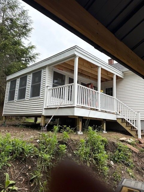 White porch addition with railing and stairs on a raised foundation, attached to a white house.