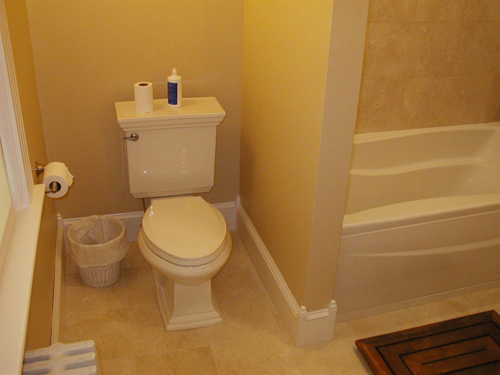 A bathroom with a toilet, trash can, and bathtub.