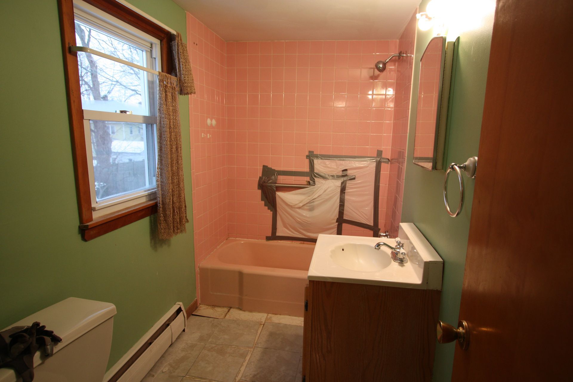 A bathroom with pink tiles, a sink, a toilet, and a window.