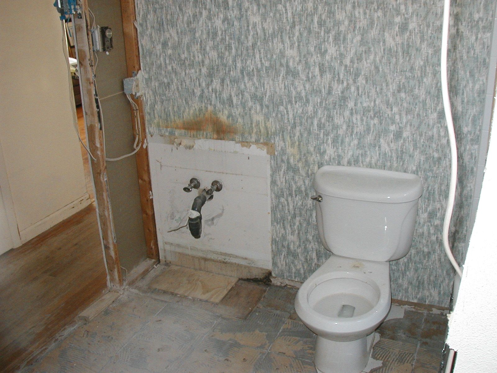 A toilet is sitting in a bathroom with a hole in the wall.