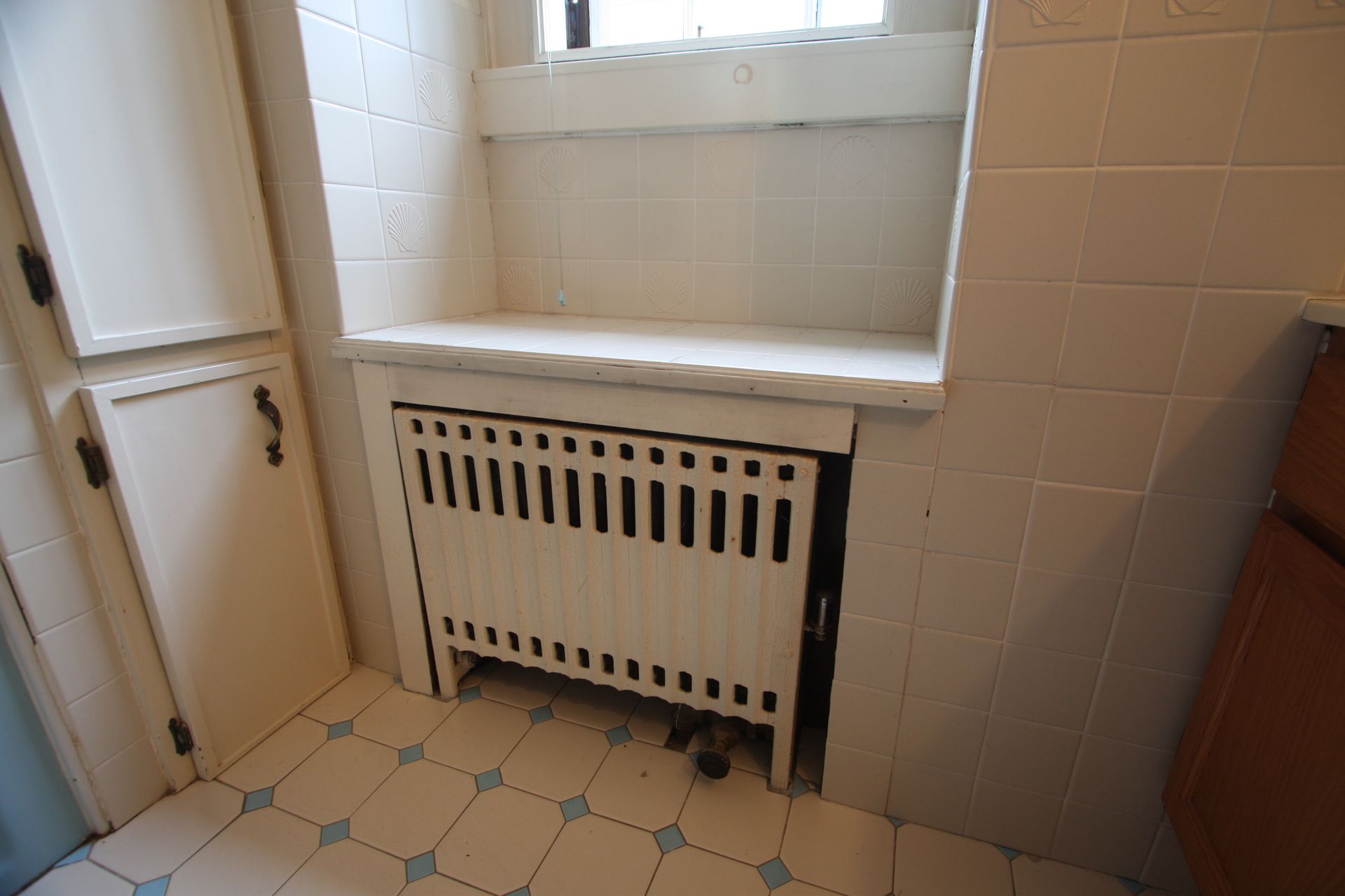 A white radiator is sitting under a window in a bathroom.