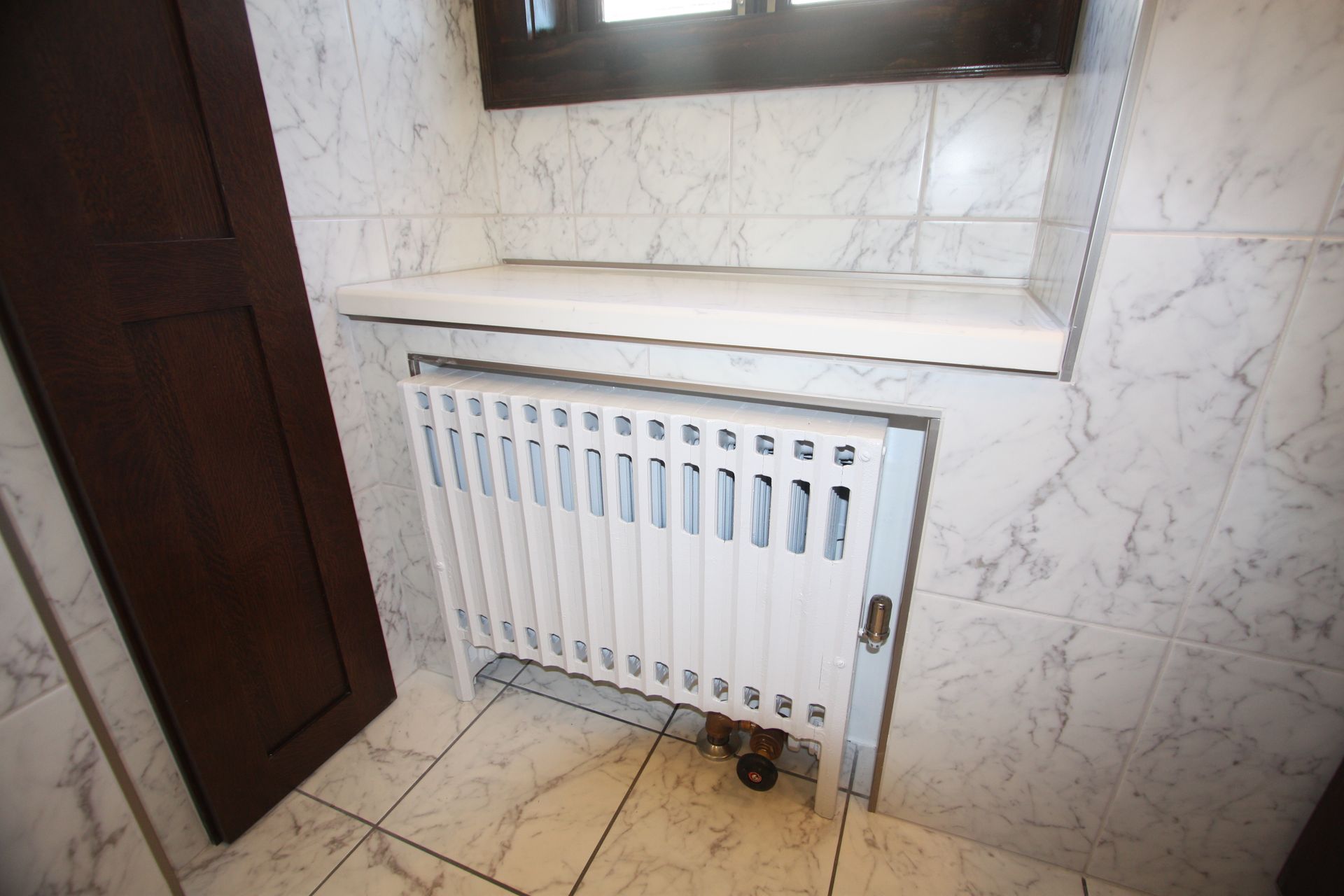 A white radiator is sitting under a window in a bathroom.