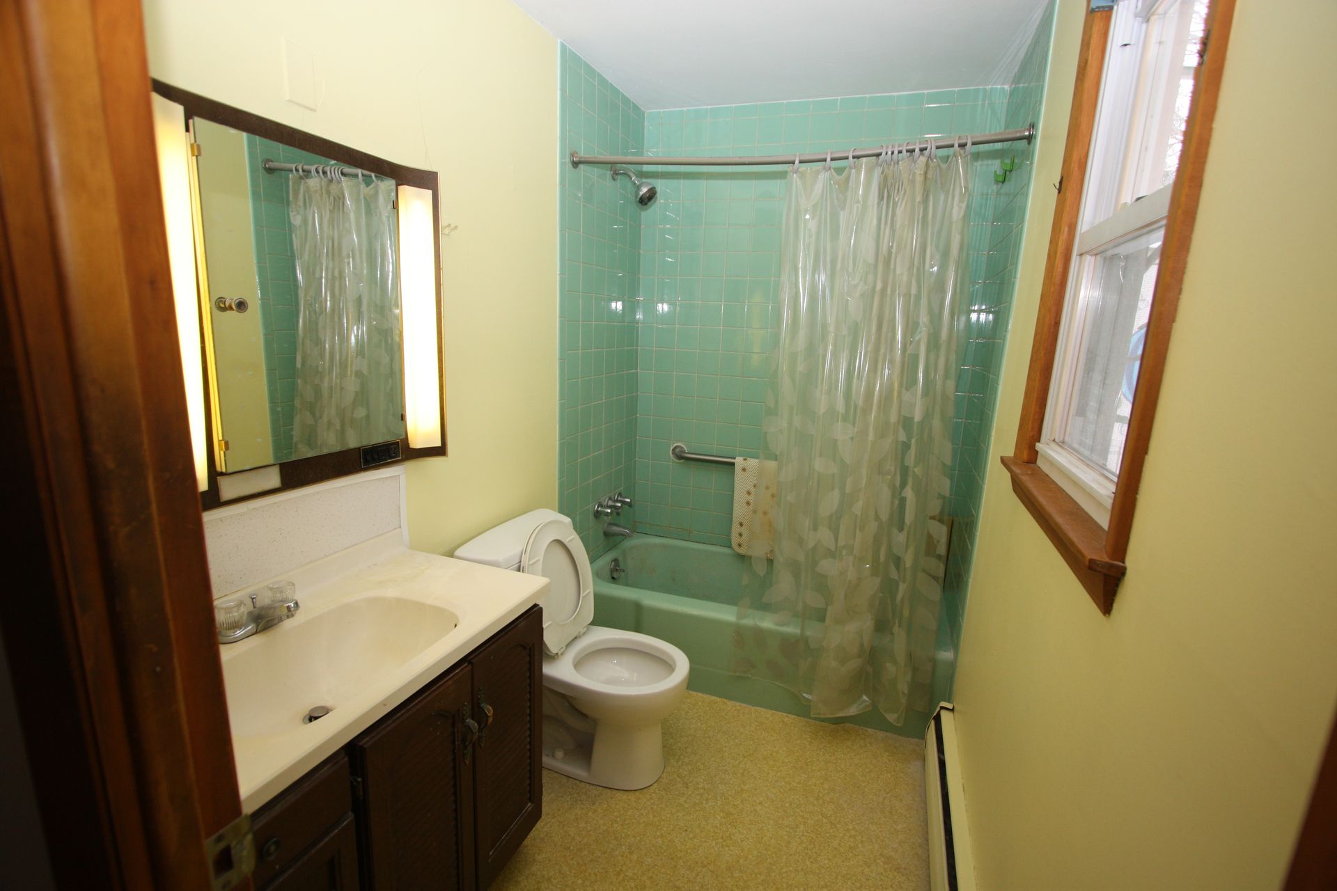 A bathroom with a toilet, sink, shower, and window.
