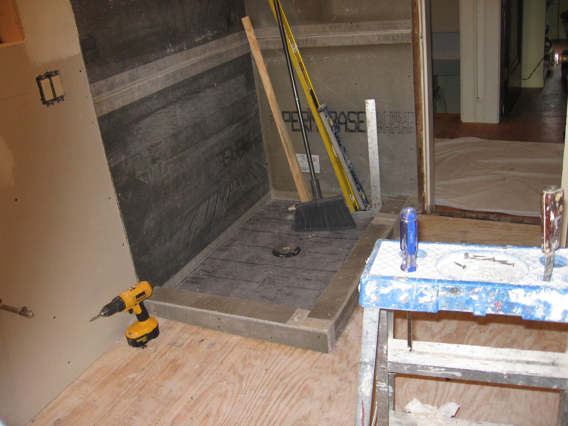 A drill is sitting on the floor next to a broom.