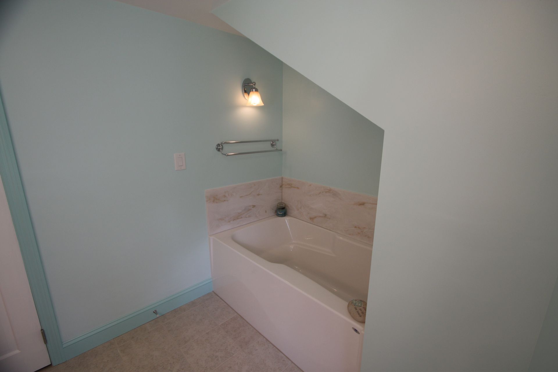 A bathroom with a bathtub under a staircase and a light on the wall.