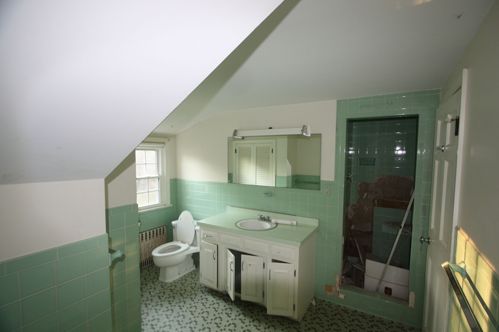 A bathroom with green tiles, a toilet, sink, and mirror.