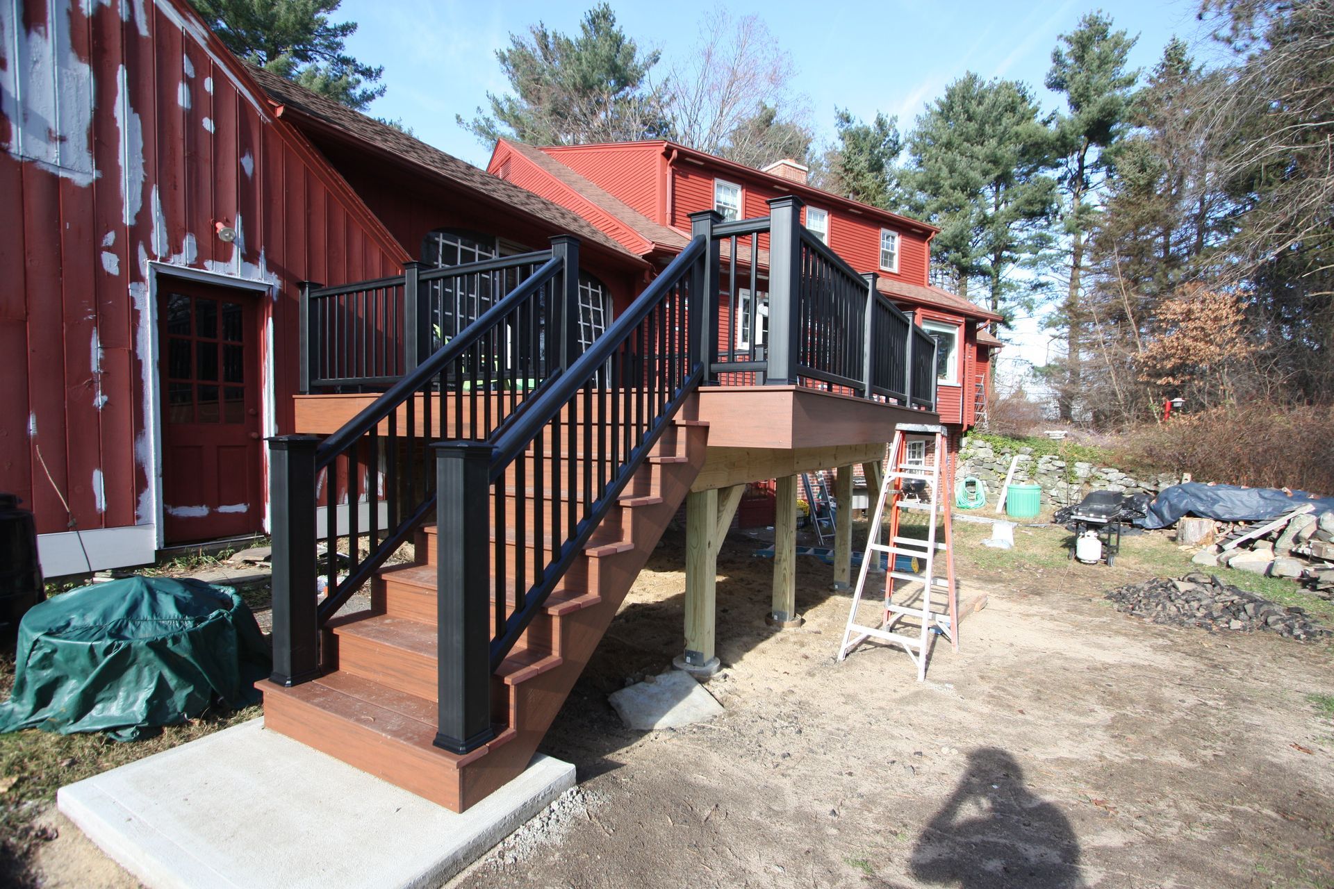 A deck with stairs and a ladder in front of a red barn.