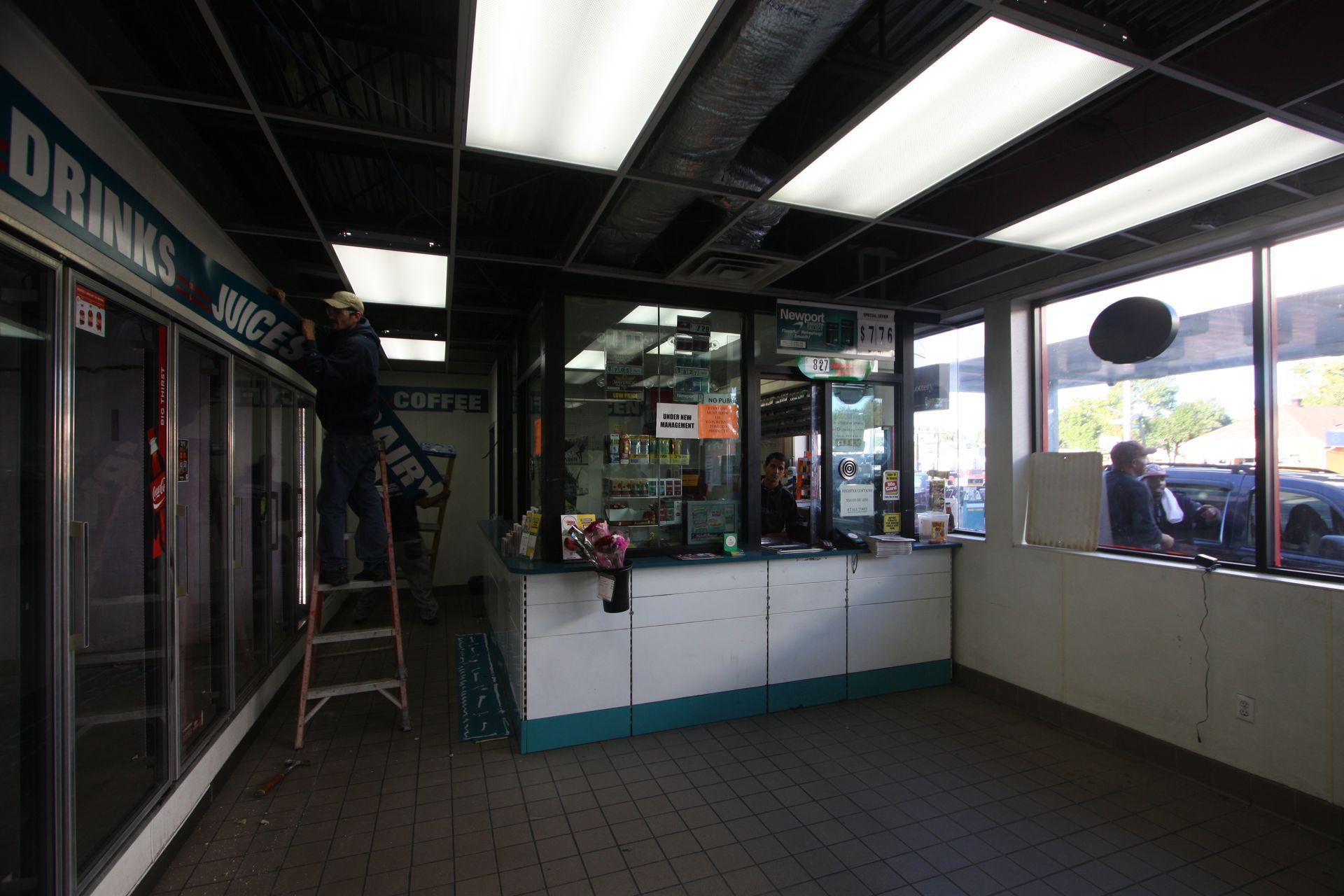 A man standing on a ladder in front of a drinks section of a store.