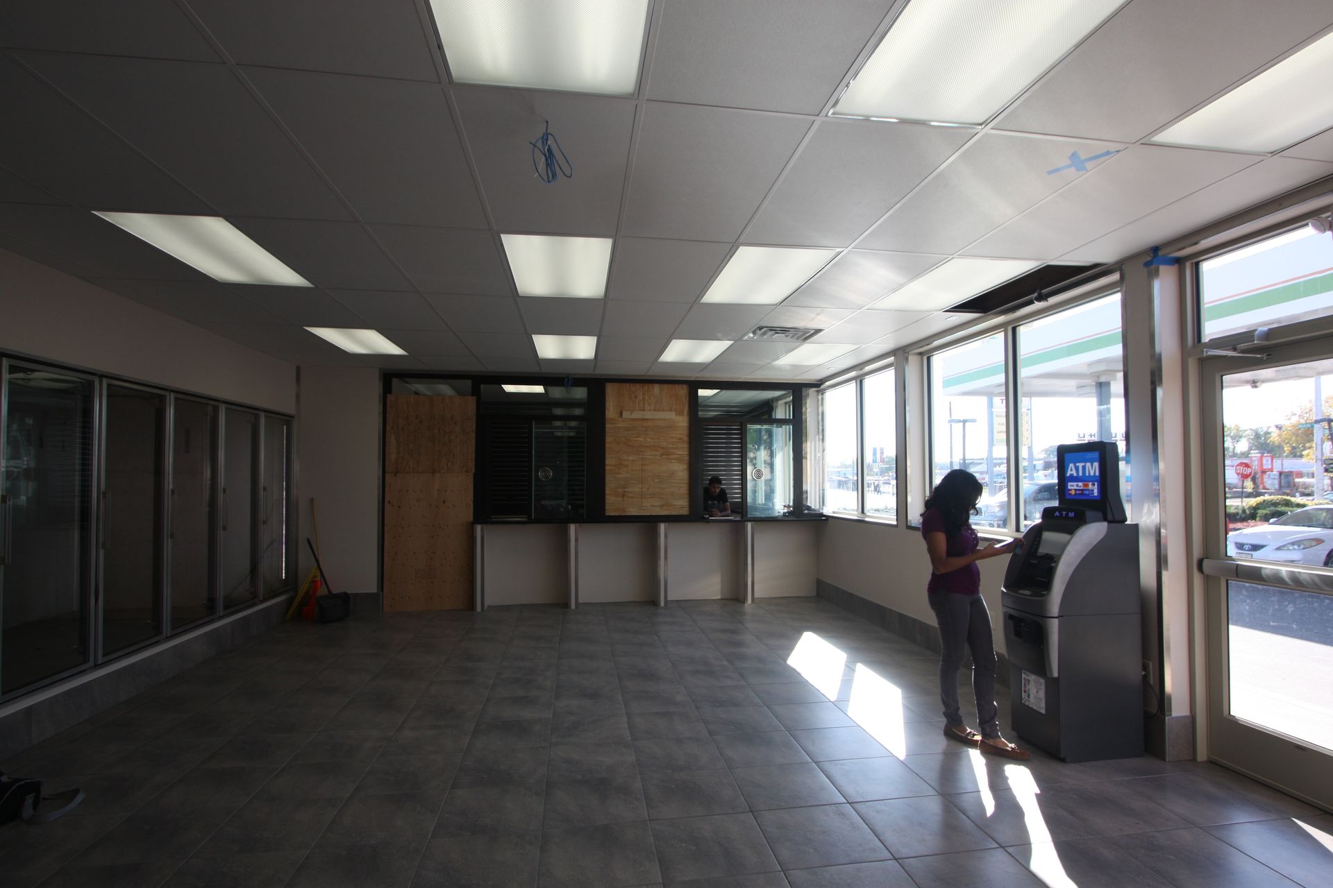 A woman is standing in an empty room next to an atm machine.