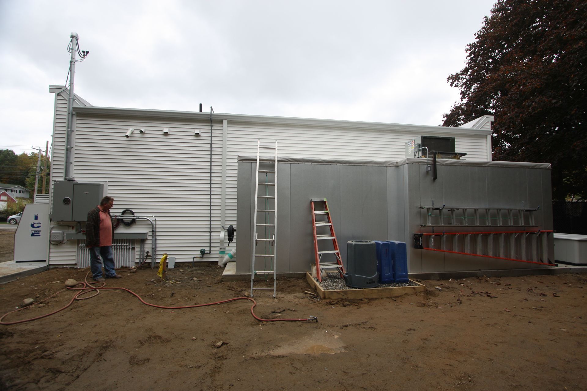 A man is standing in front of a building with a ladder on the side.