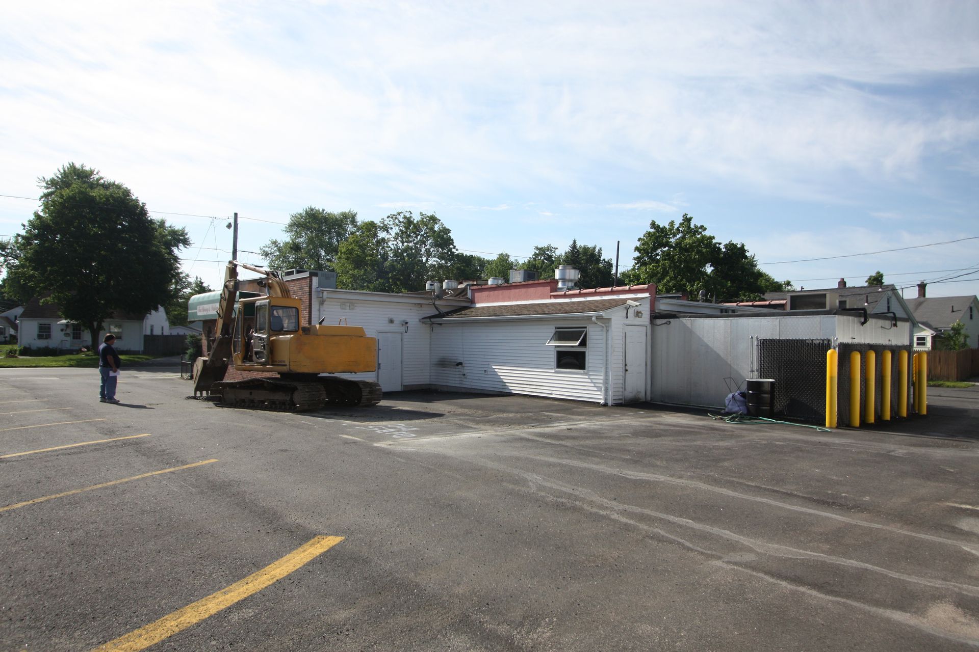 A yellow excavator is parked in front of a white building.
