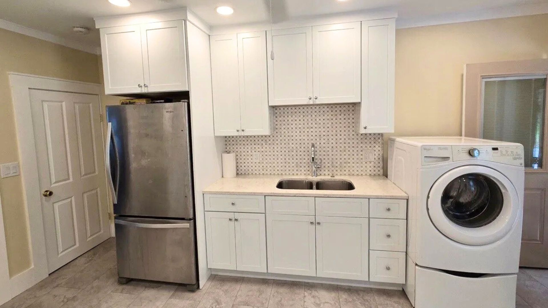 Small white kitchen with stainless fridge, white cabinets, and a washer on the right side.