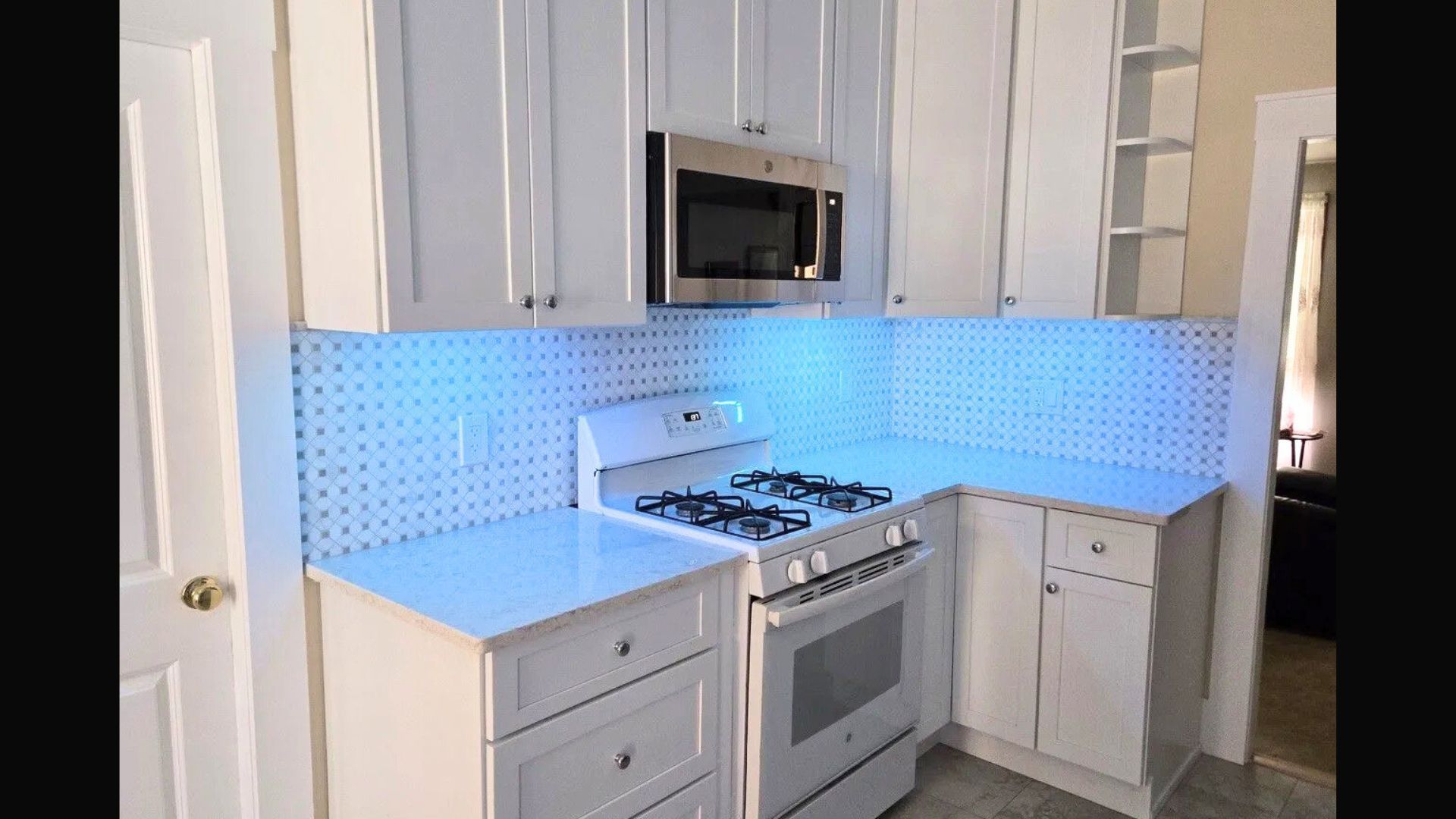 Modern white kitchen with blue tile backsplash, stainless appliances, and corner countertops.