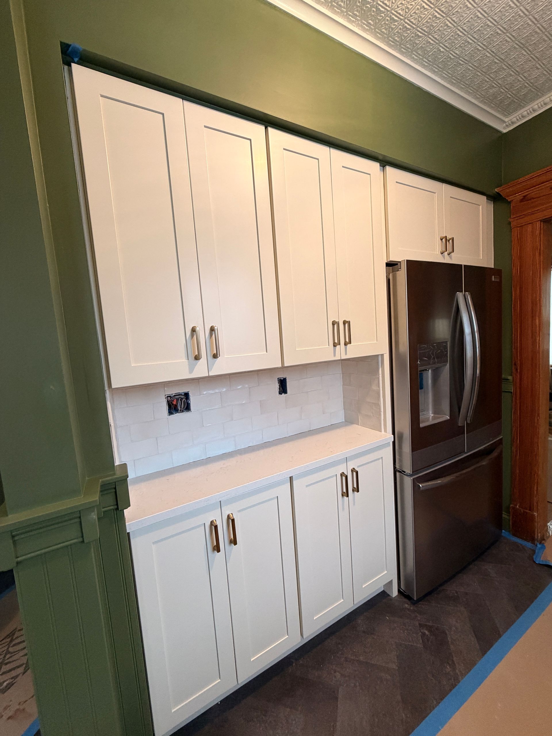 White kitchen cabinets and dark refrigerator against a green wall in a small kitchen.