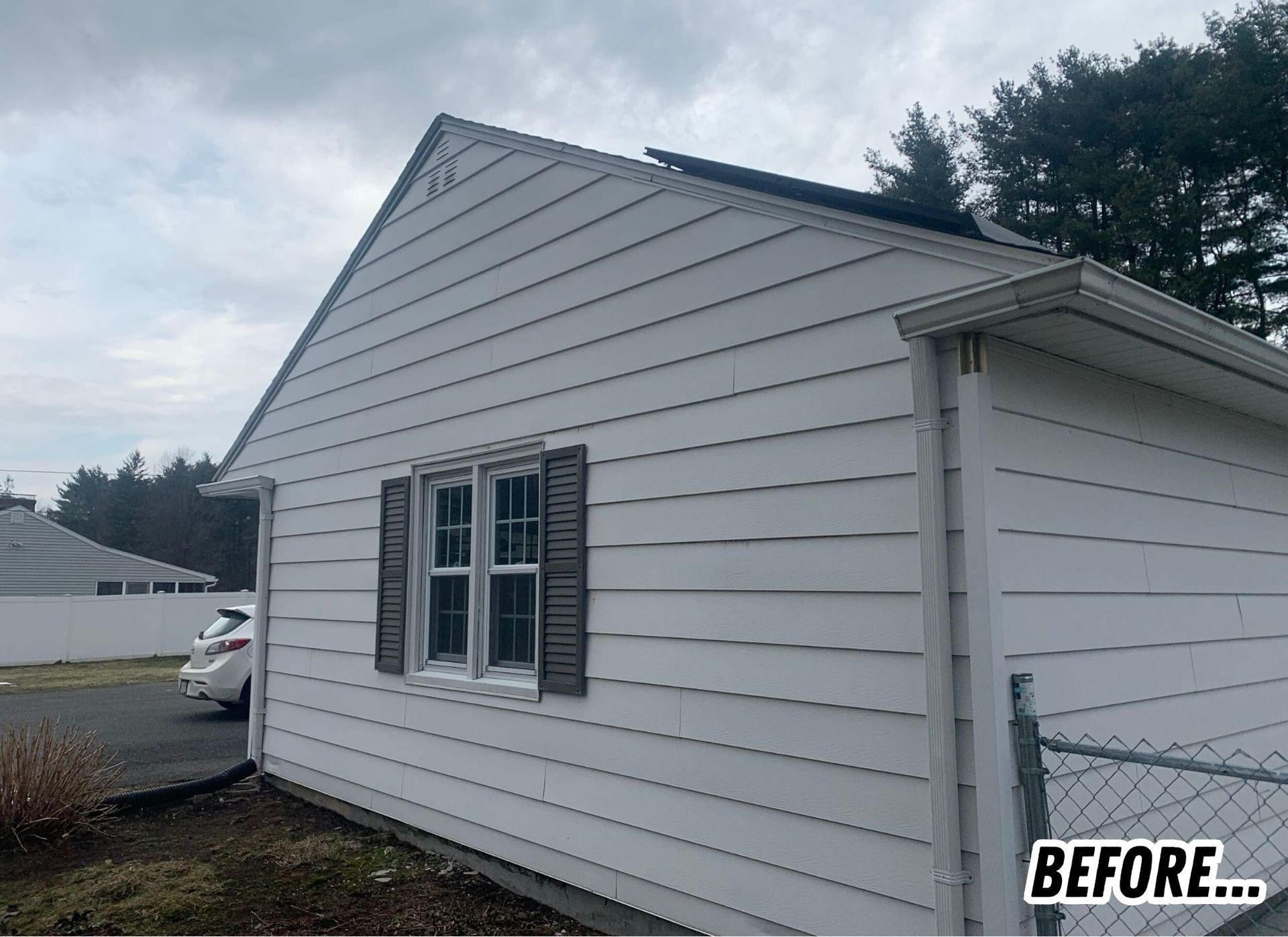 White house exterior with gray siding, window shutters, and cloudy sky; BEFORE label in corner