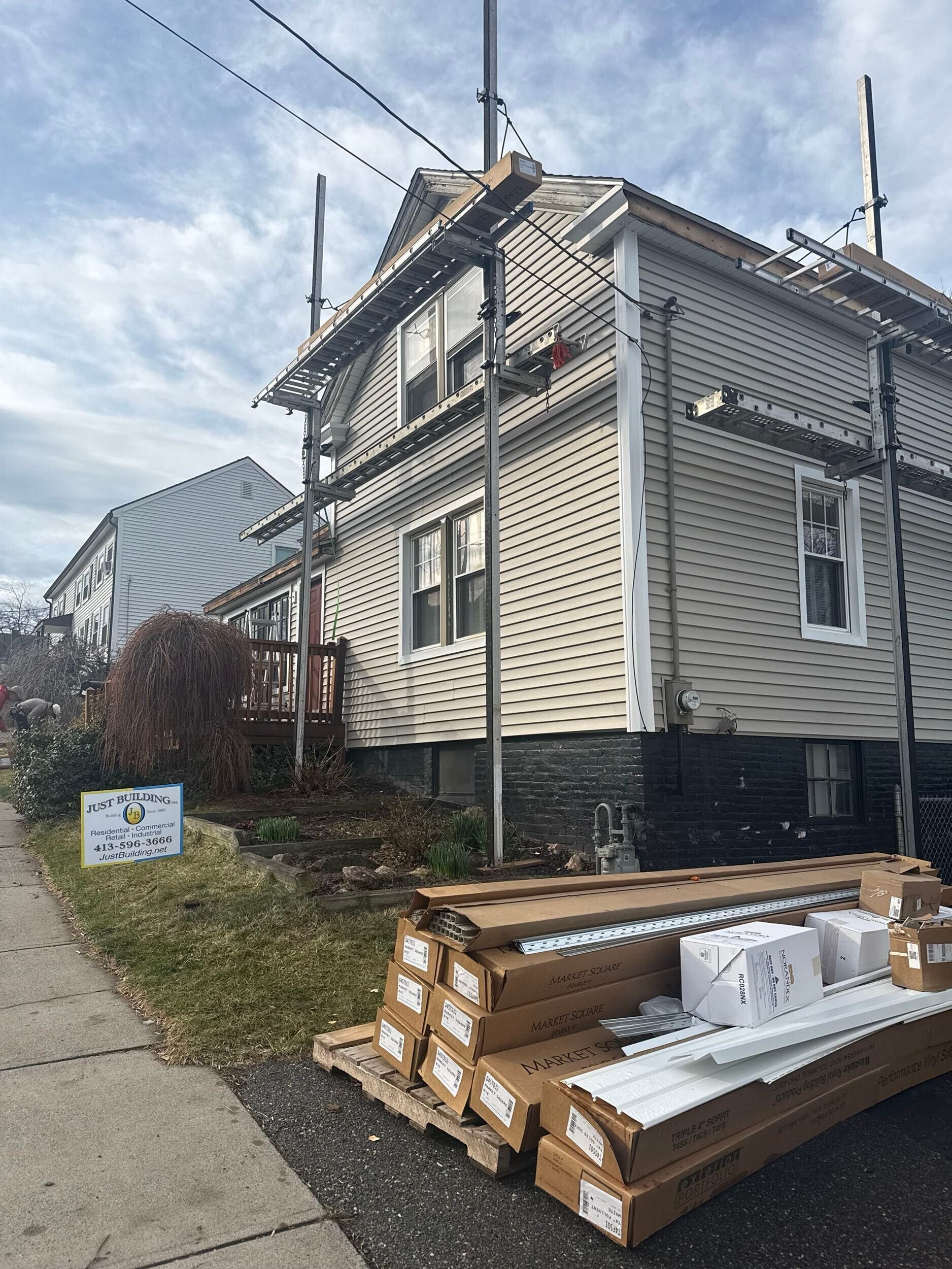 House under construction with stacked lumber and building materials beside a sidewalk